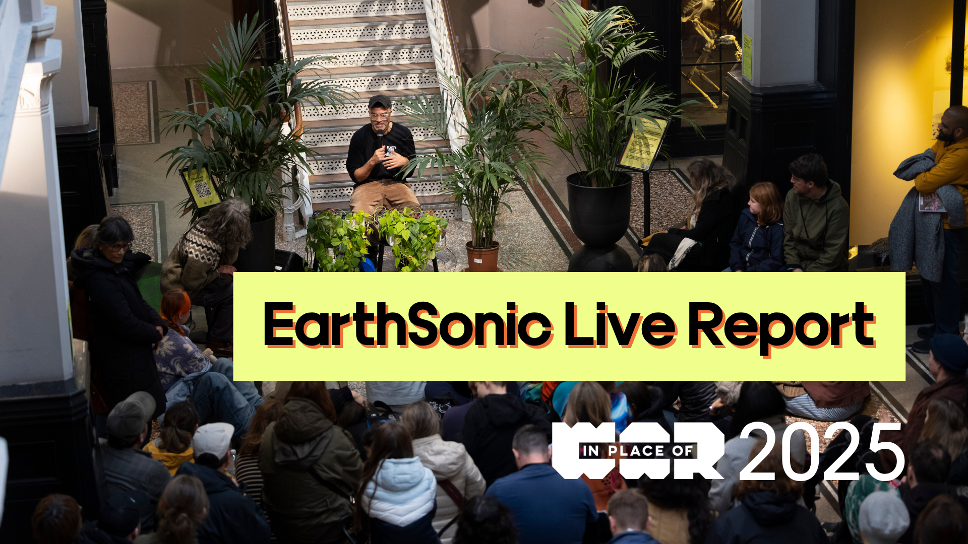 A photo of a man speaking into a microphone in front of a crowd at Manchester Museum. Text overlaid reads: EarthSonic Live Report 2025, with the In Place of War logo.