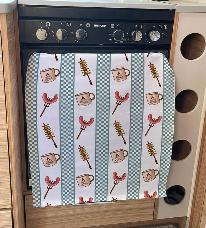 Striped tea towel decorated with sausages, kebabs and camping mugs.