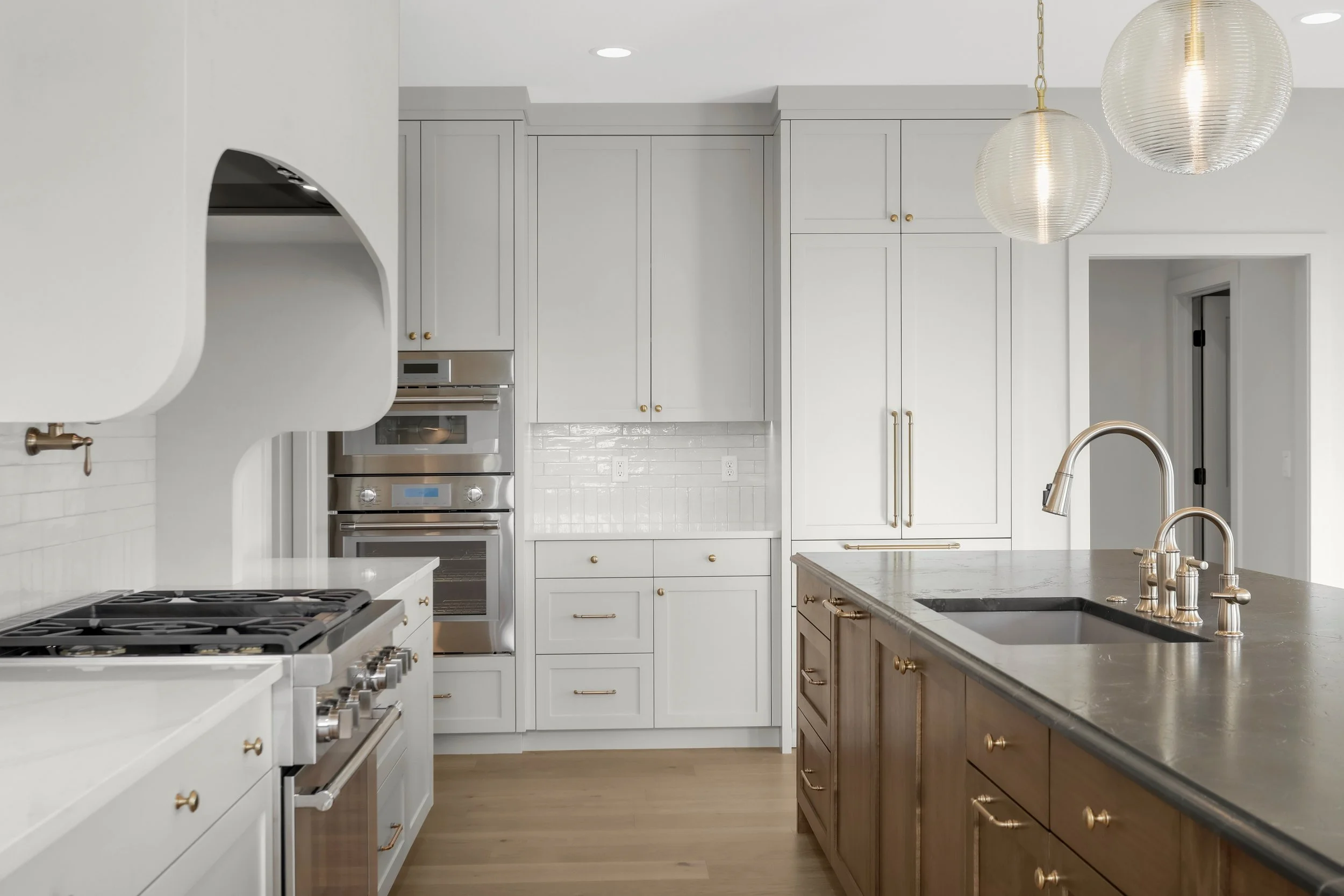 Bright modern kitchen with white cabinets, stainless steel appliances, marble island, farmhouse sink, brass fixtures, and pendant lights
