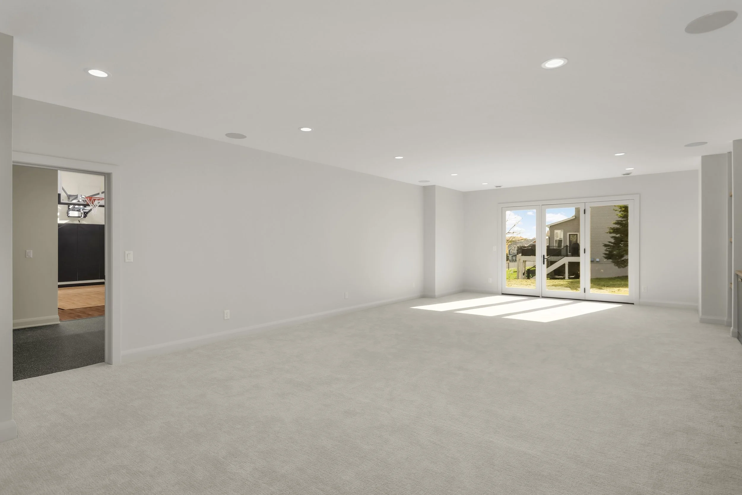 Bright finished basement with carpeted floors, recessed lighting, French doors to the backyard, and a nearby basketball court