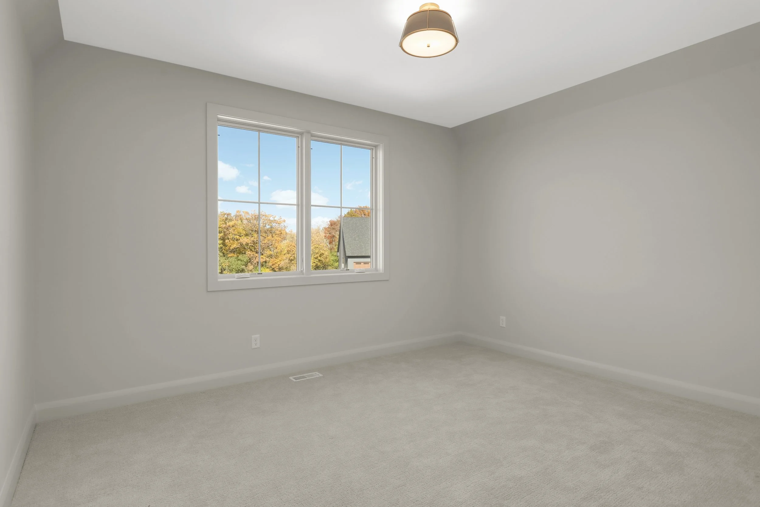 Empty carpeted bedroom with gray walls, a ceiling light, and double window overlooking autumn trees