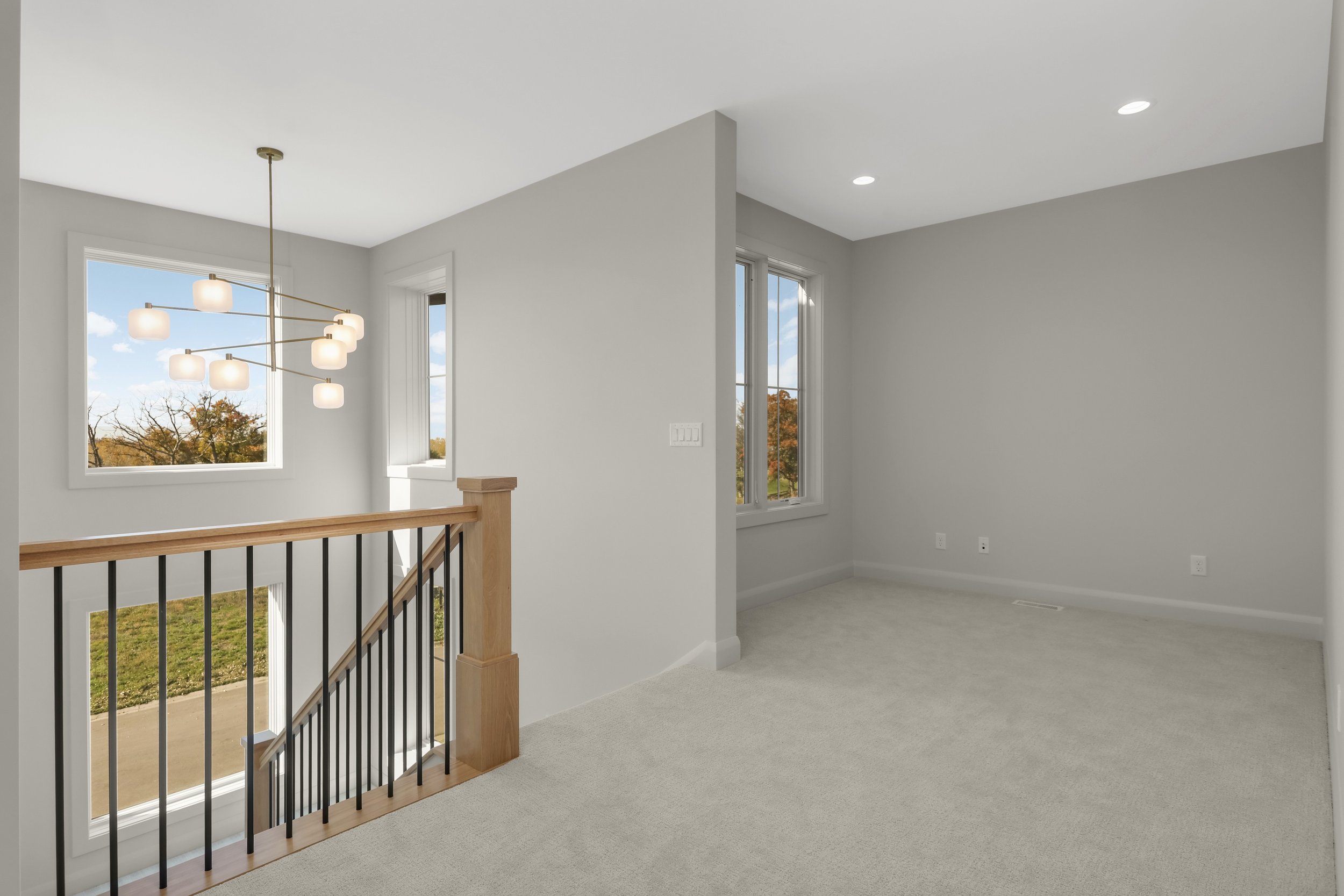 Bright carpeted upstairs home interior with large windows, modern pendant light, and wood-and-black stair railing.