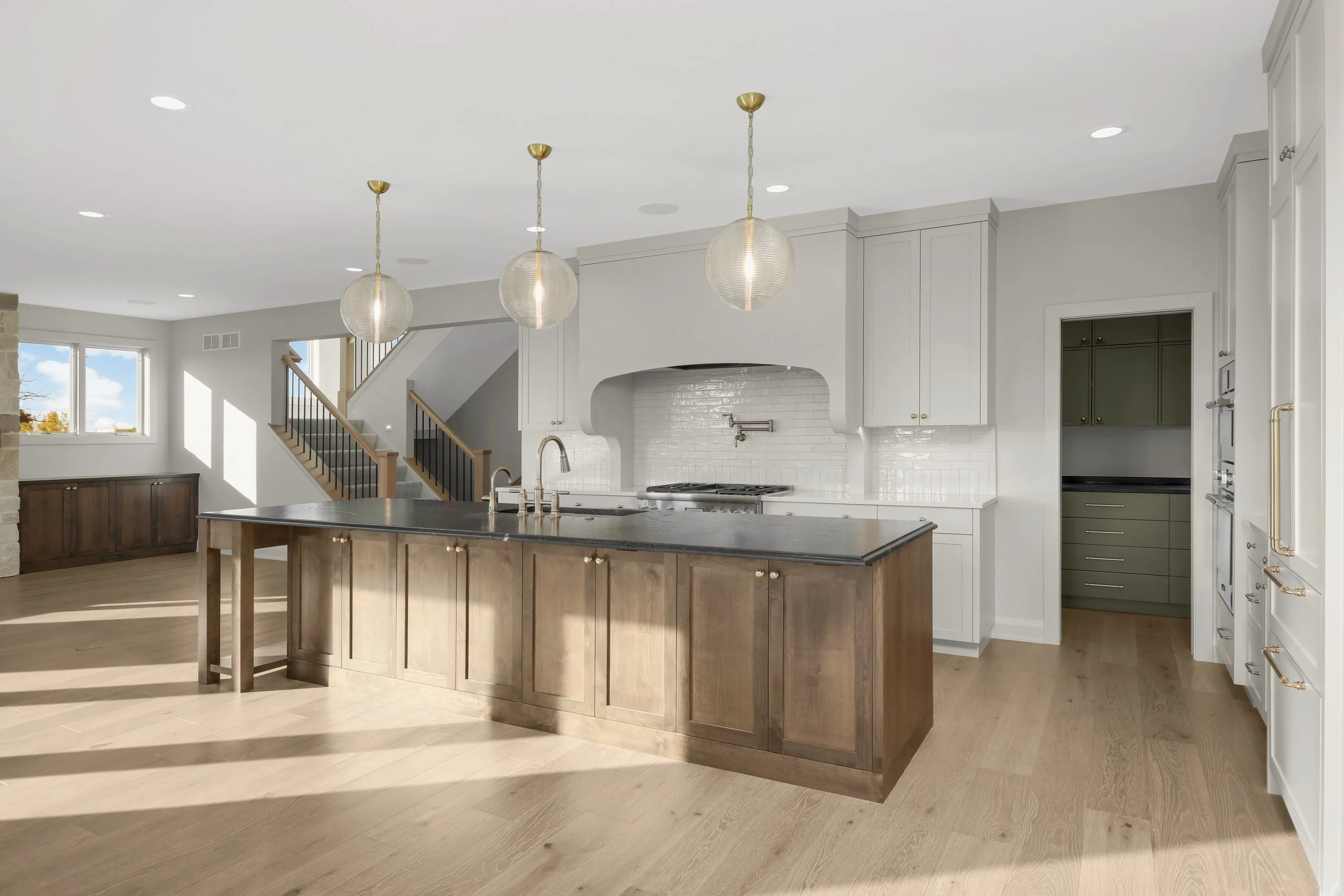 Bright modern kitchen with a large wood island, white cabinetry, subway tile backsplash, brass pendant lights, and walk-in pantry.