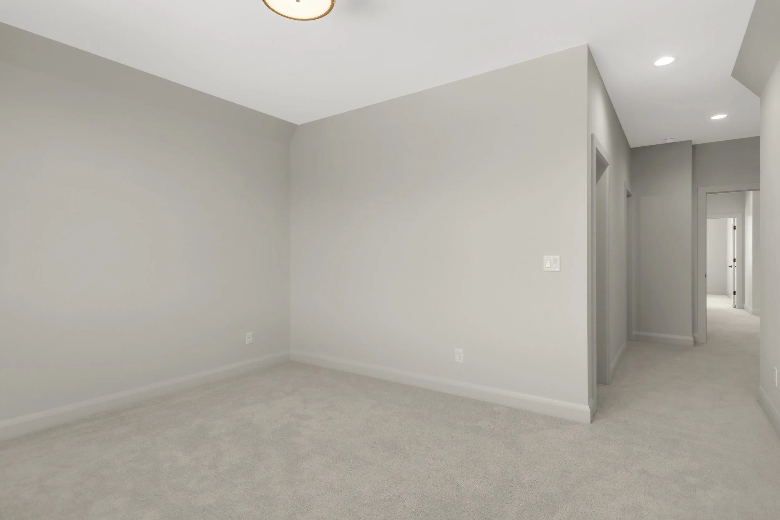 Empty carpeted room with light gray walls, recessed lighting, and hallway doorways