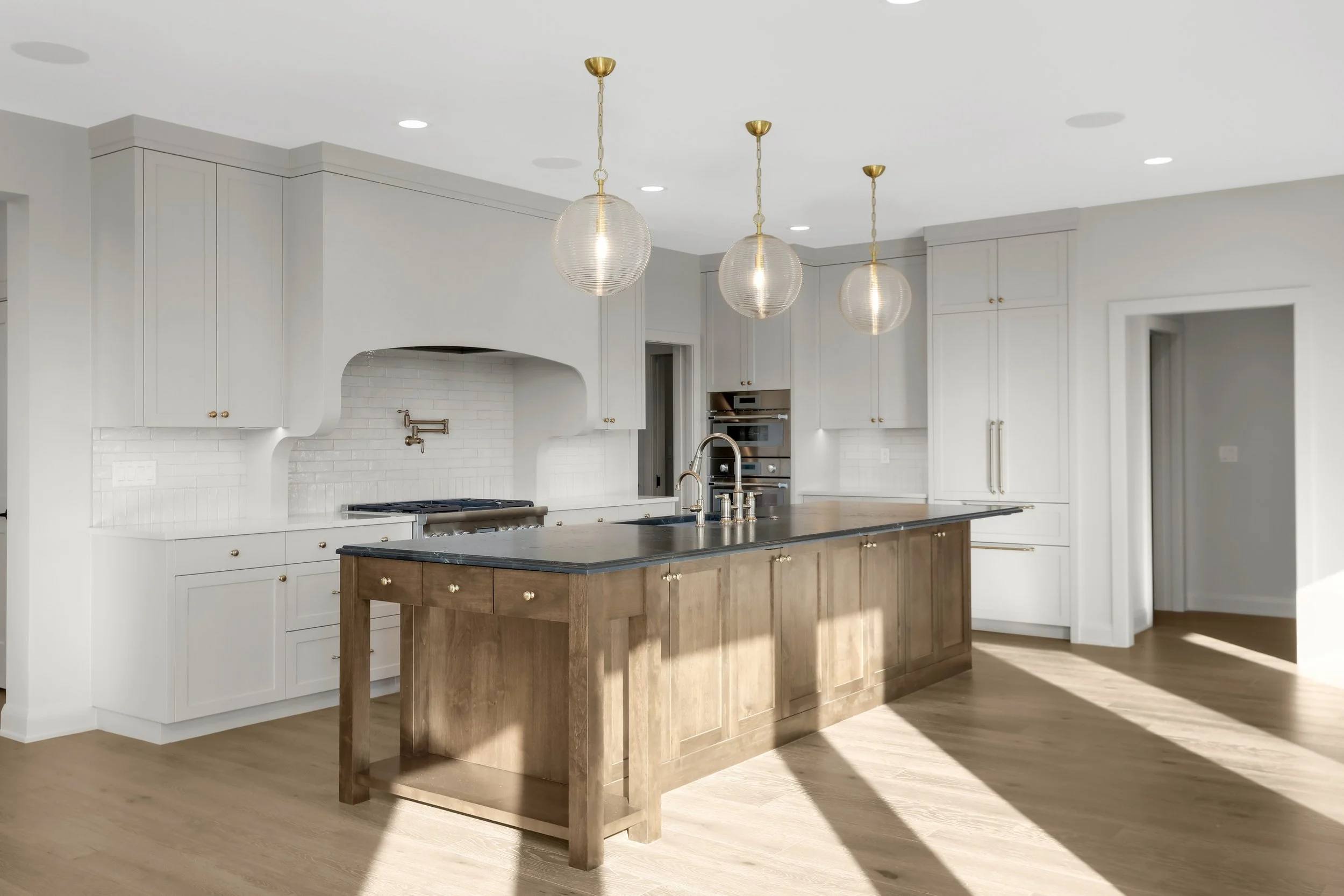 Bright modern kitchen with white cabinetry, wood island, black countertops, subway tile backsplash, stainless-steel appliances, and three globe pendant lights