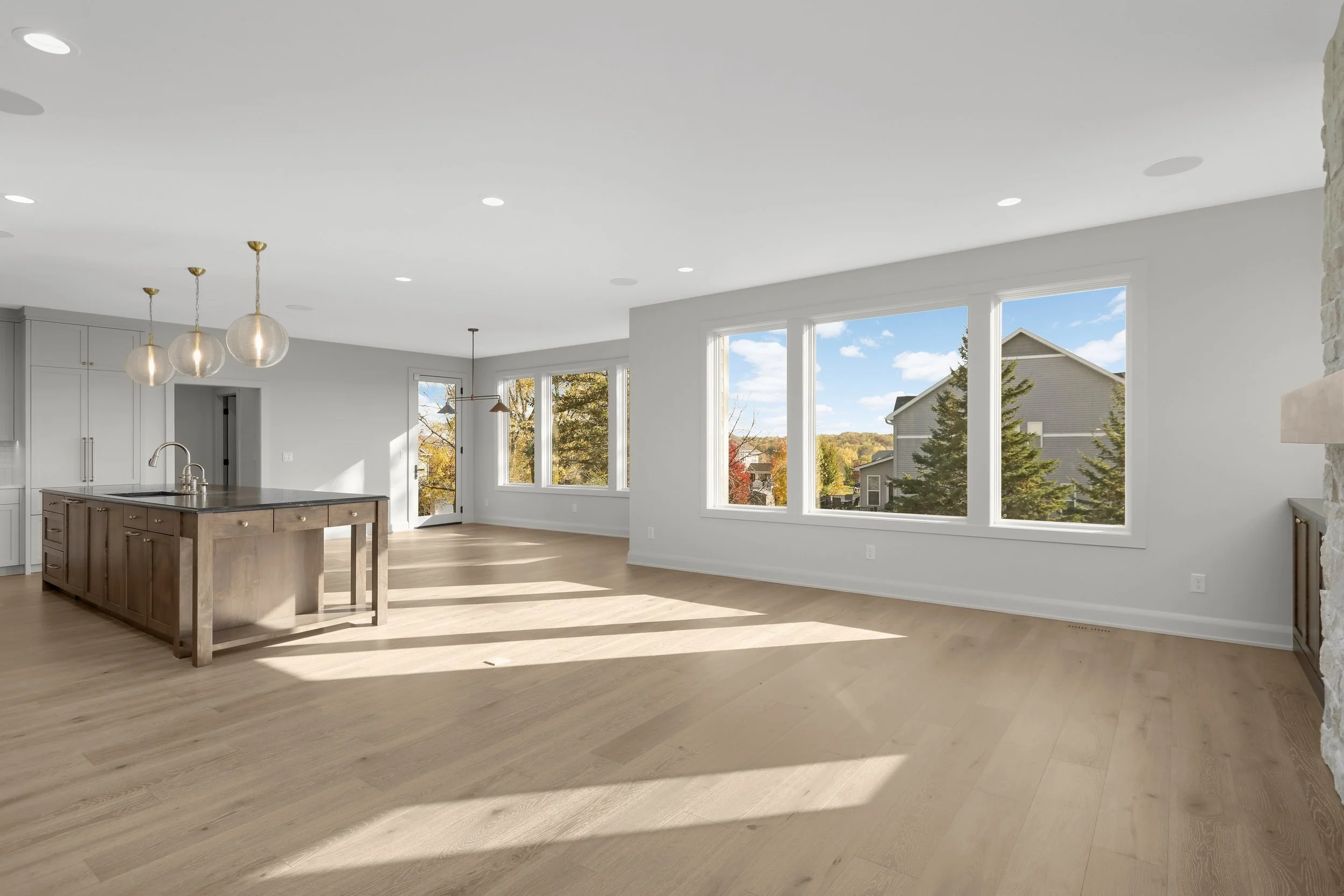 Bright open-concept kitchen and living area with a large island, pendant lights, hardwood floors, and expansive windows overlooking a residential neighborhood.