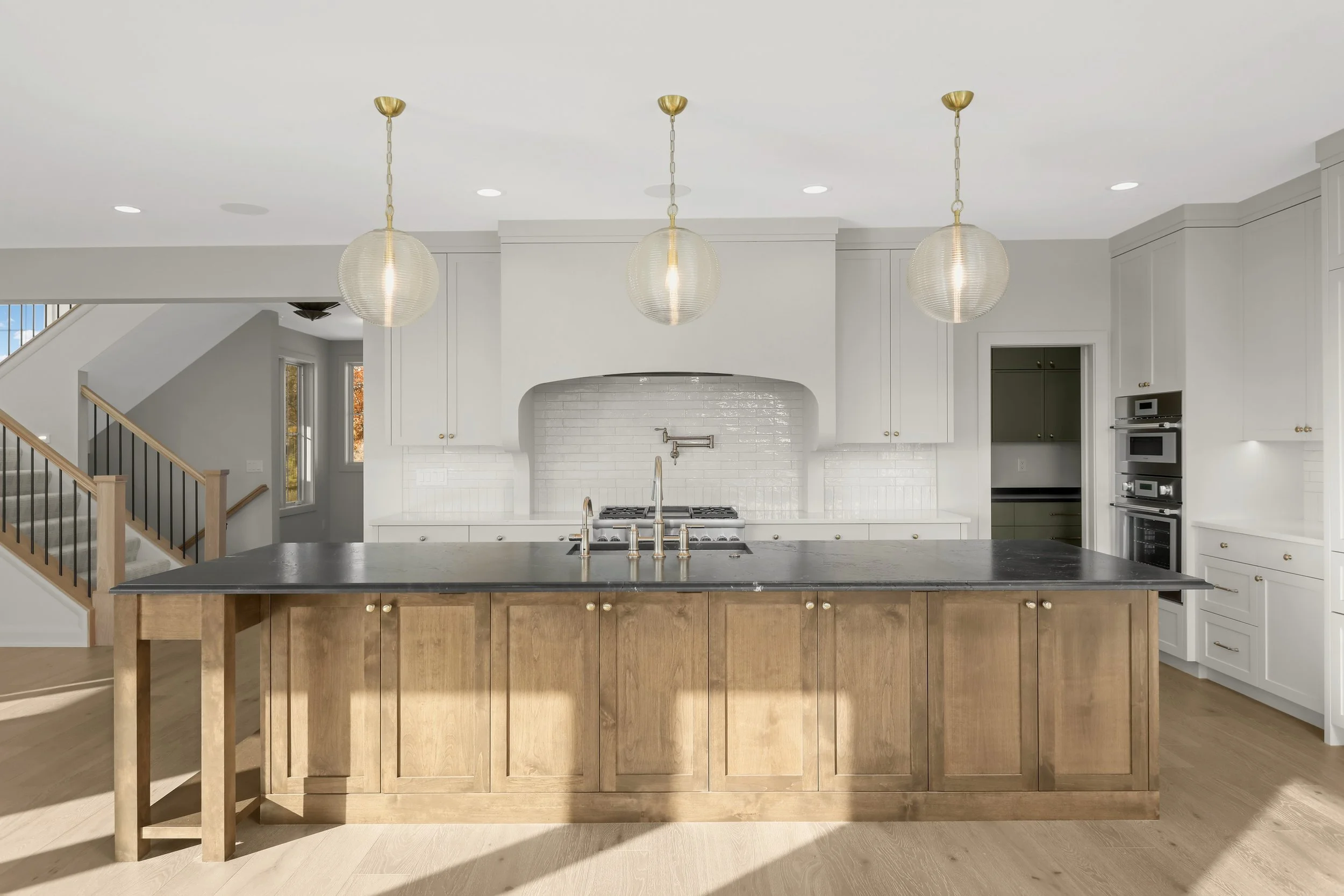 Bright modern white kitchen with a large wood island, black countertop, pendant lights, white subway tile backsplash, and stainless steel appliances