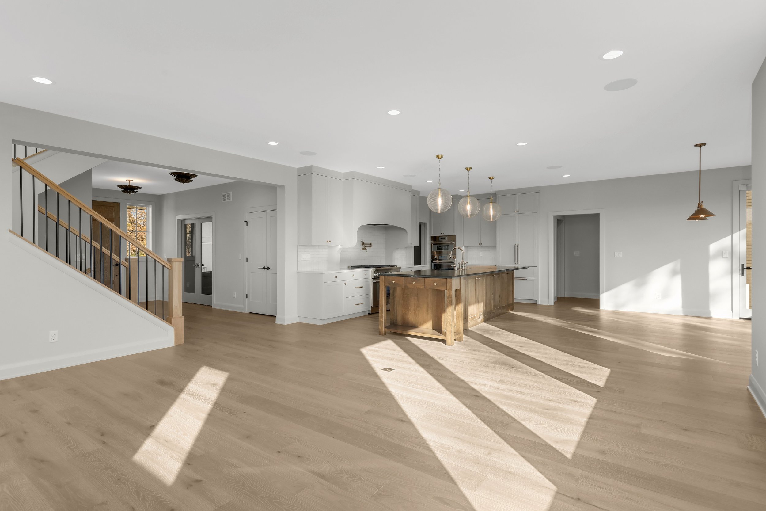 Bright open-concept kitchen and living area with a wood island, white cabinetry, hardwood floors, pendant lights, and staircase