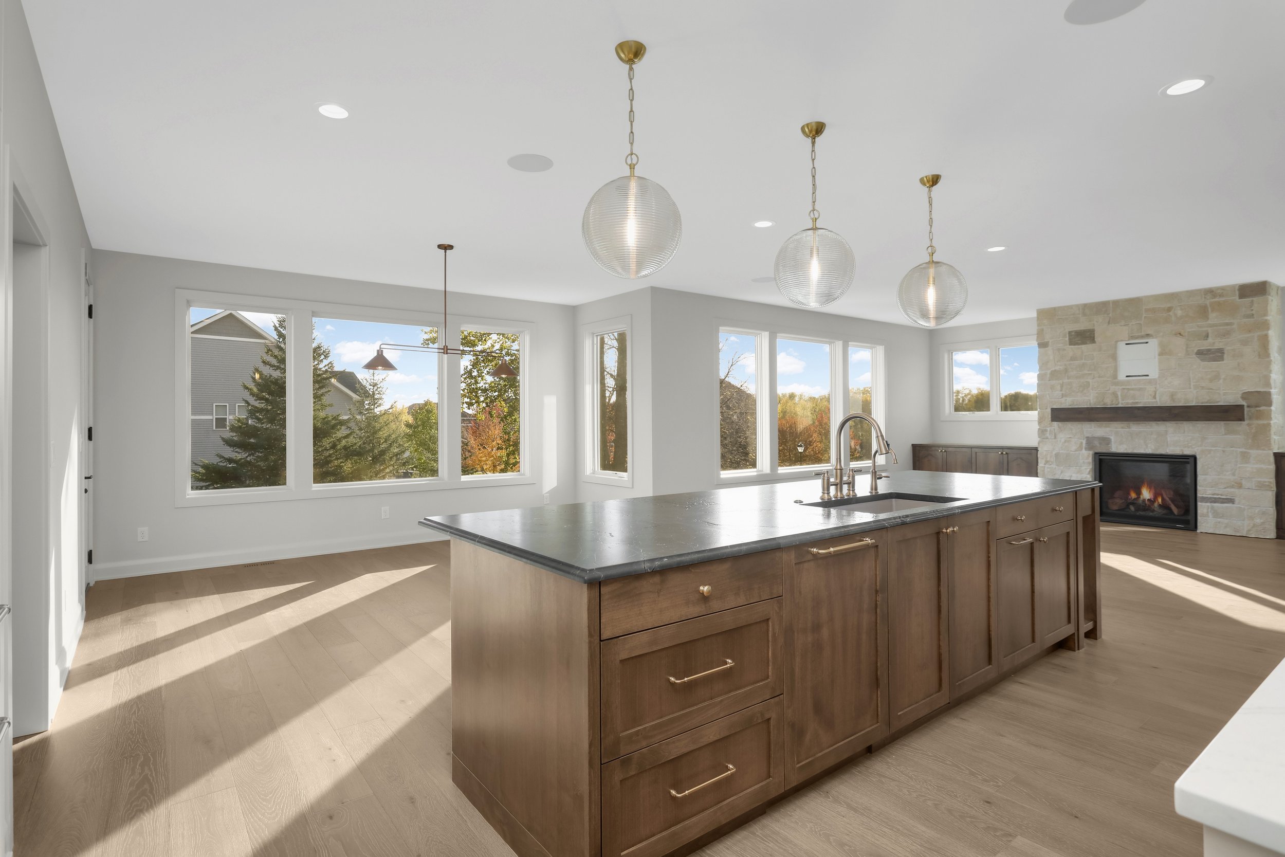 Bright modern kitchen with a large wood island, pendant lights, expansive windows, and a stone fireplace