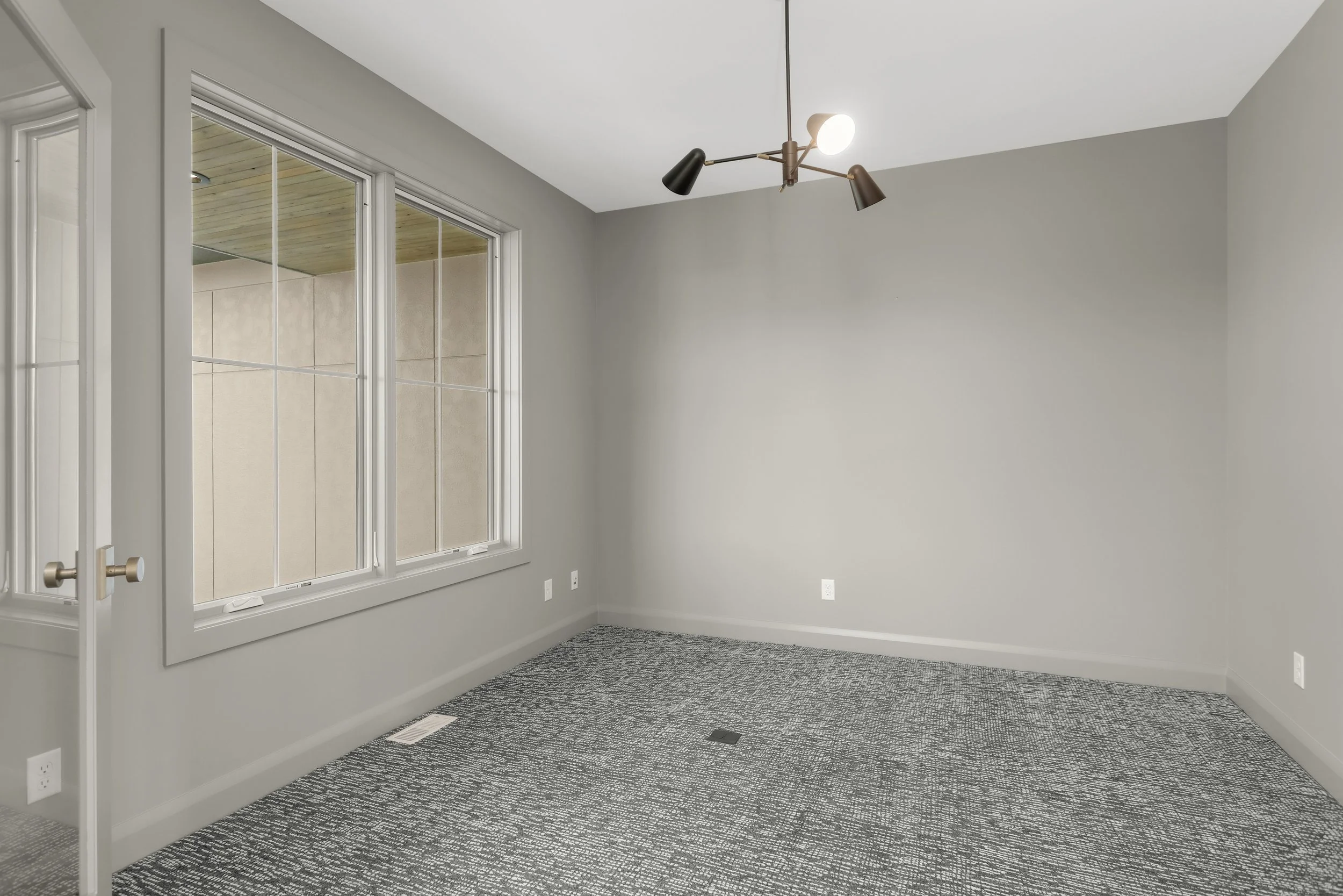 Empty gray-carpeted room with large windows, a glass-paneled door, and modern ceiling light fixture