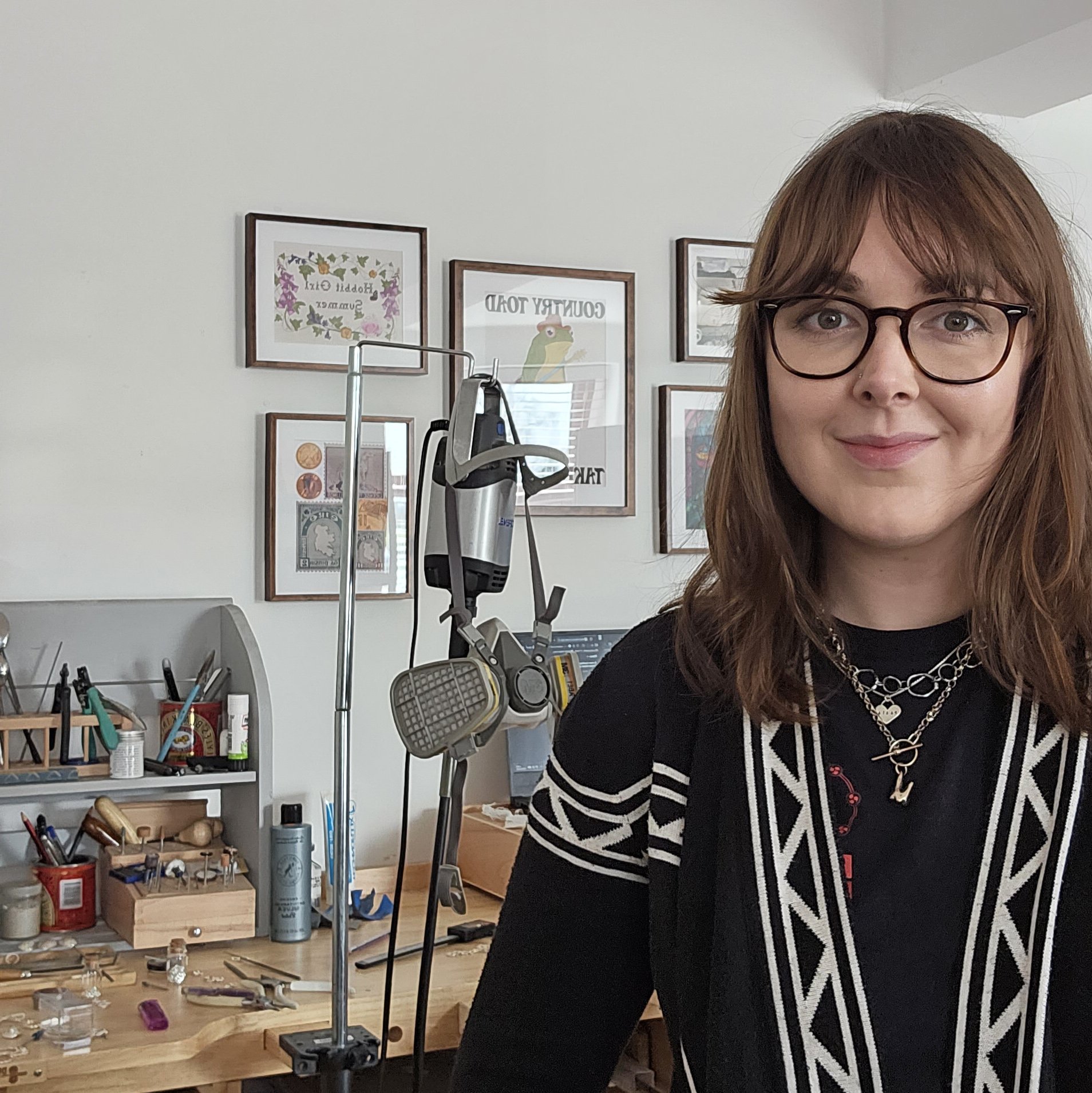 A photo of the jeweller Barbara Blane in her Northern Ireland studio. She is standing in front of her desk which has a selection of hand tools sitting ready to use.