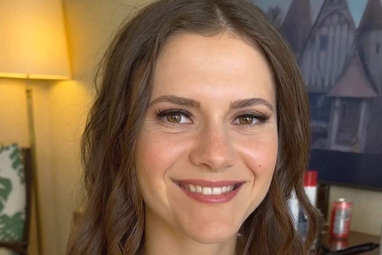 Close-up of a woman's face with light makeup, long hair, and neutral expression.