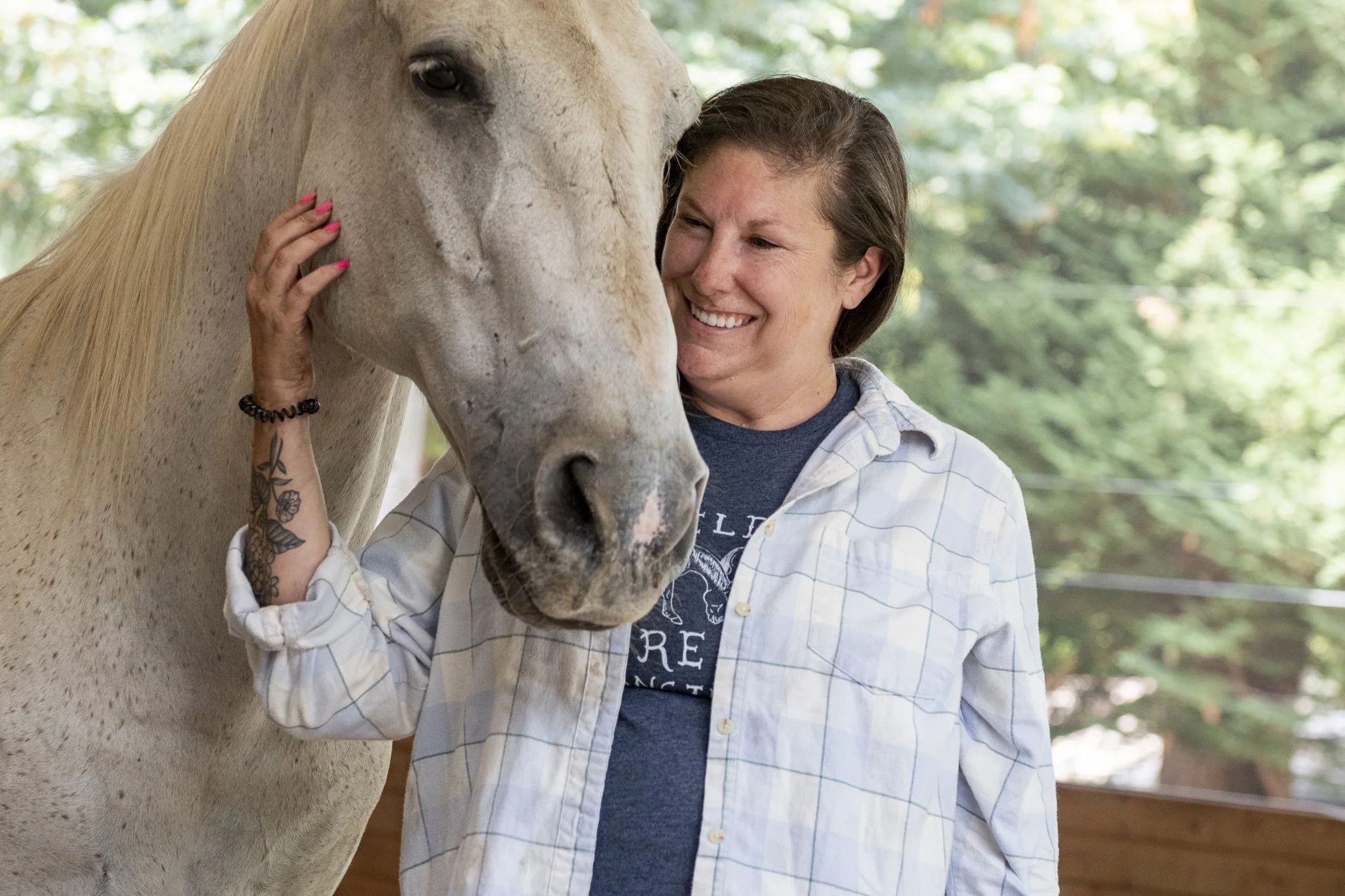 A smiling woman doing equine therapy with a grey horse