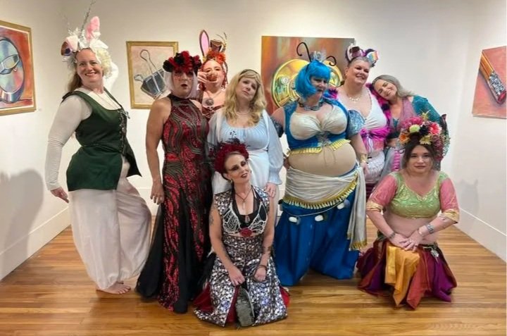 Sassy Belles student troupe in colorful Alice in Wonderlandcostumes posing together in an art gallery