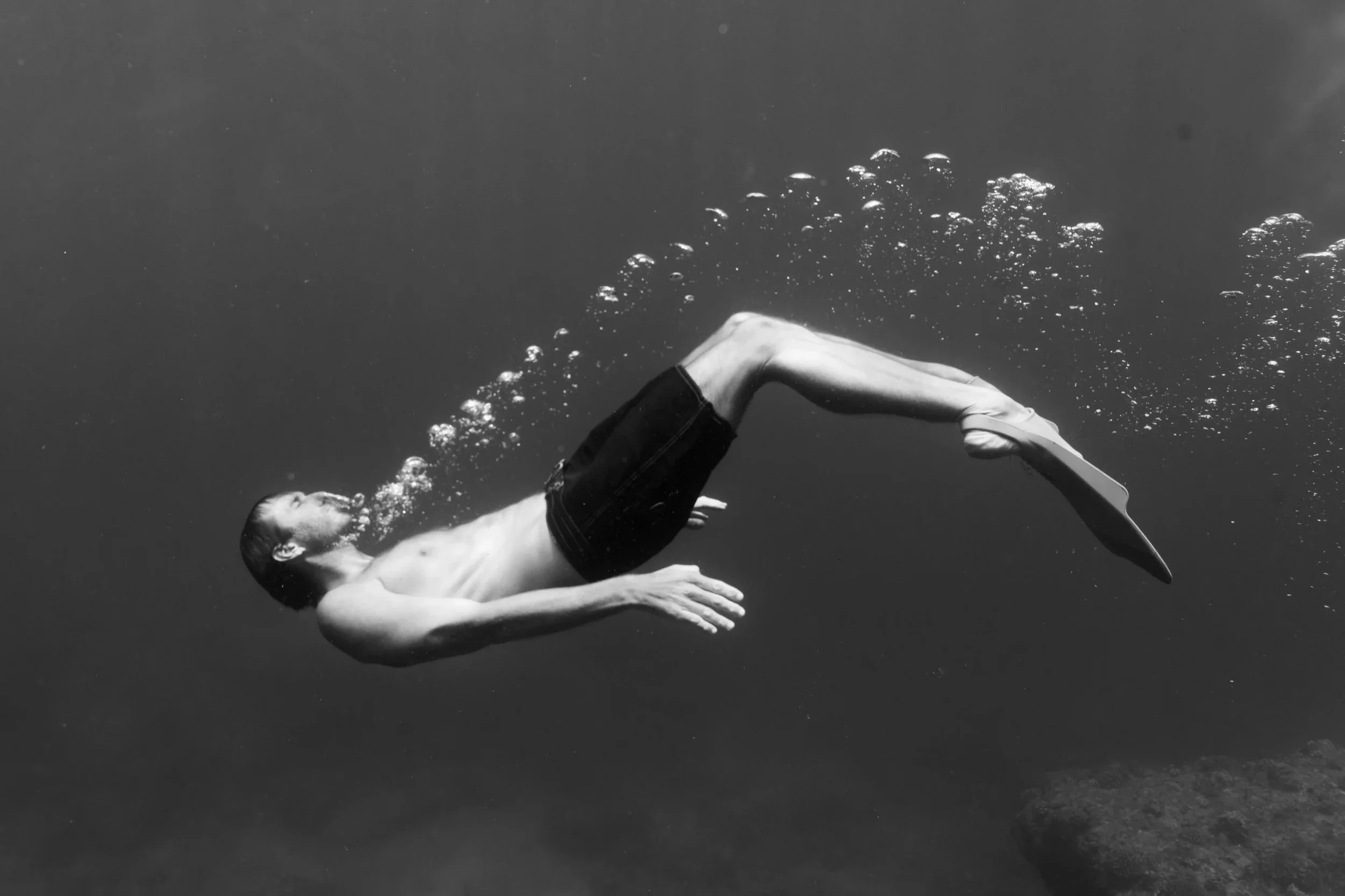A person swimming underwater, captured from the side, with water bubbles surrounding them, in a black-and-white photograph.