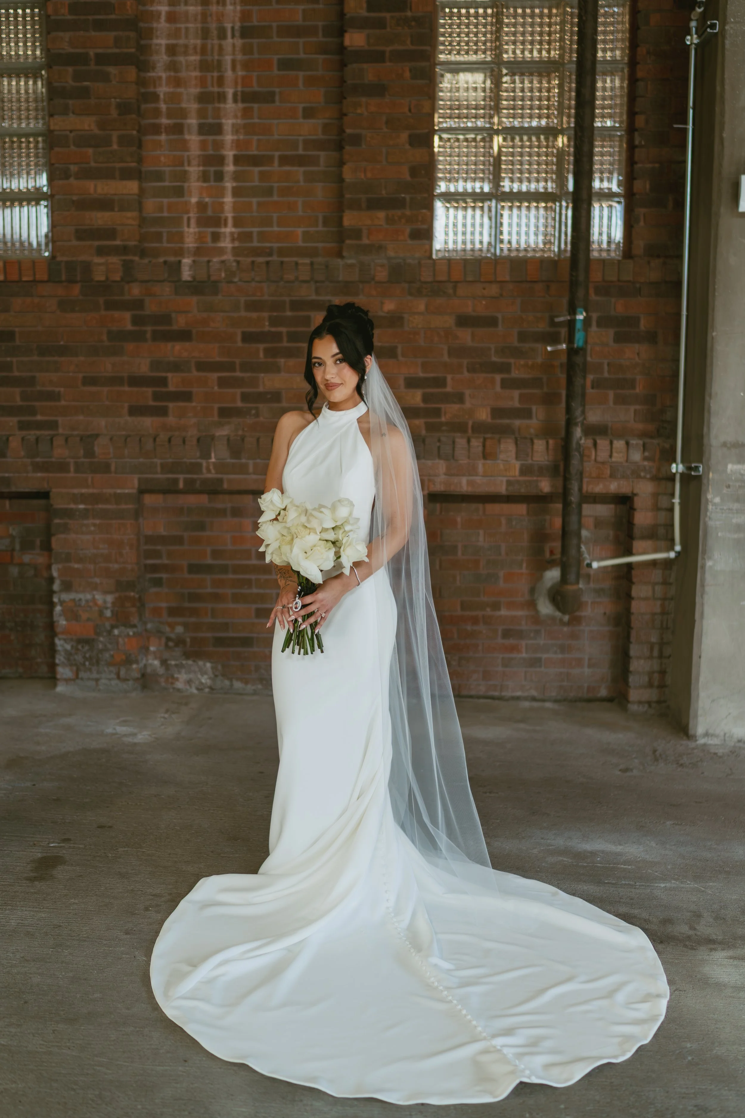  bride in brick building posing for photo smiling at the camera holding her bouquet  