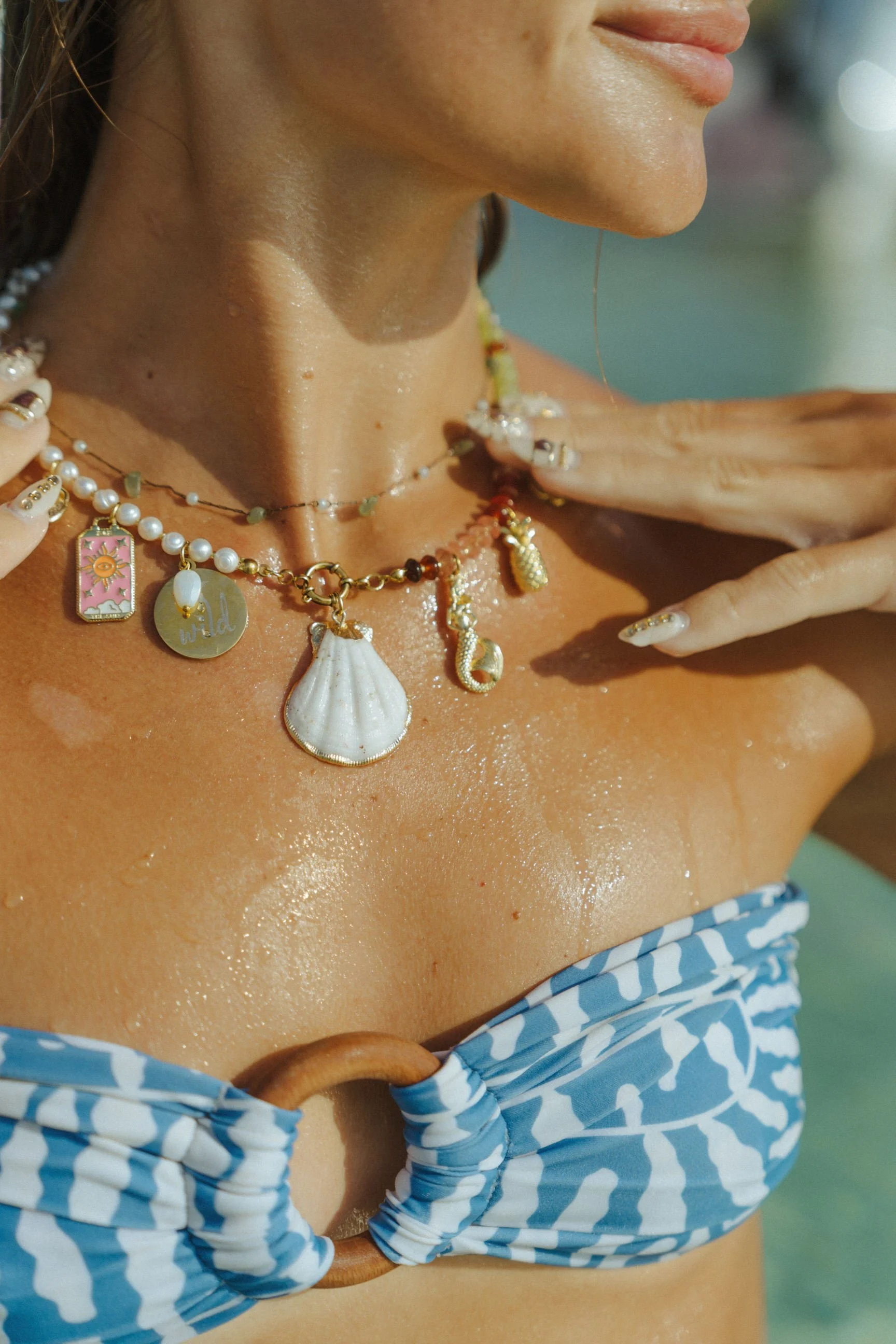 close up of beach inspired jewelry and charms with woman model in blue bikini