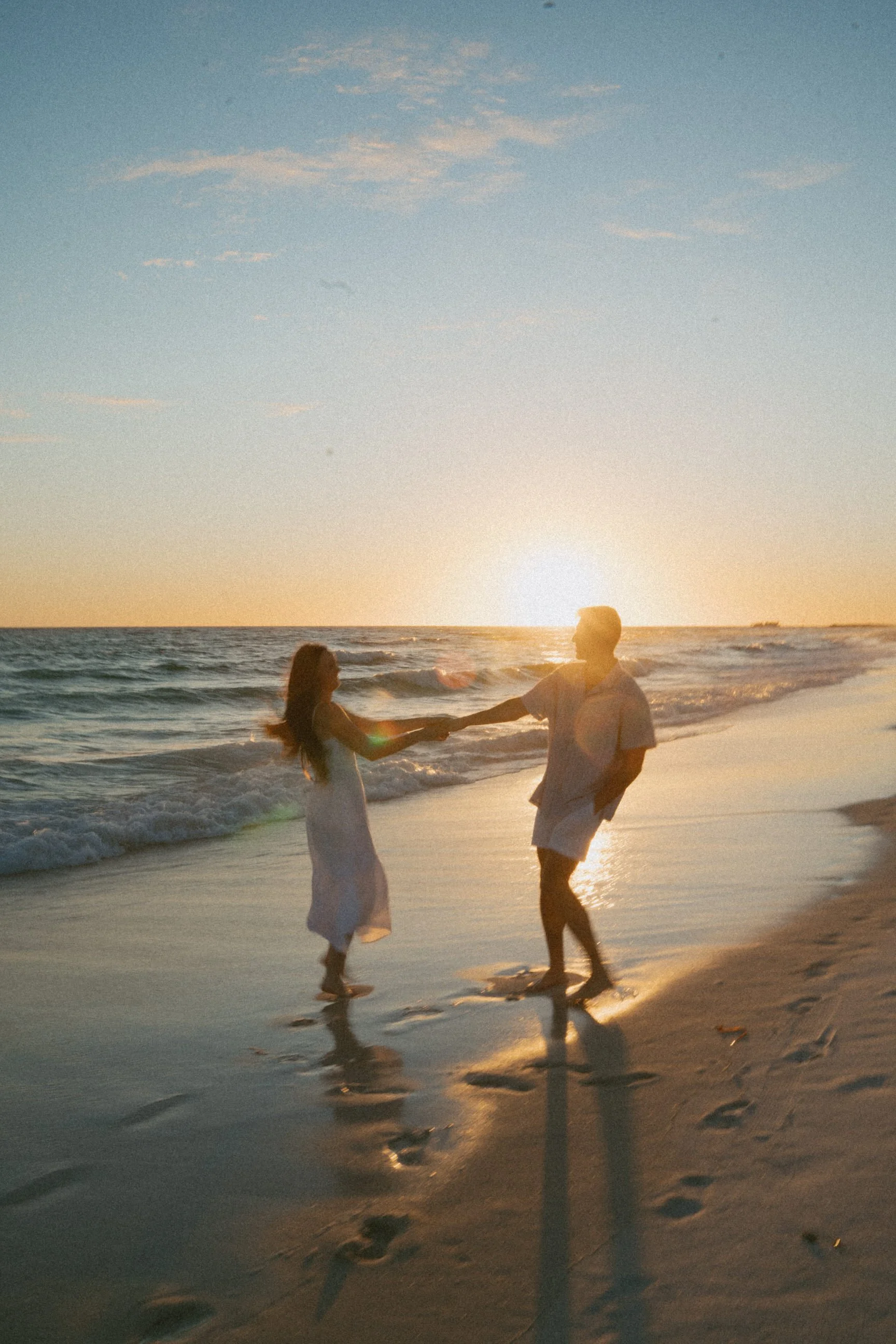 couple holding hands and spinning at the beach at sunset