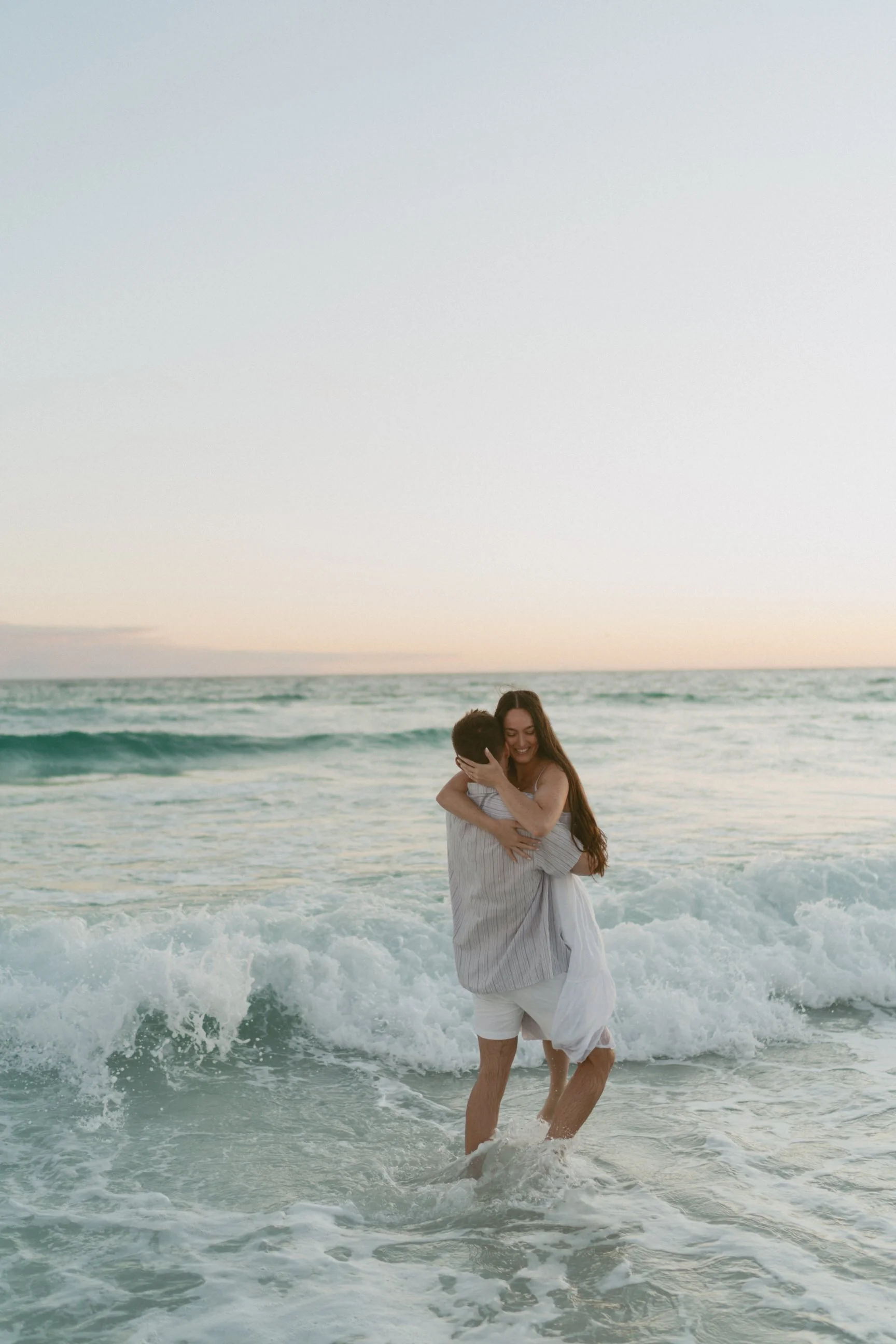 A couple at the beach embracing in the shallow water with waves, during sunset or sunrise.