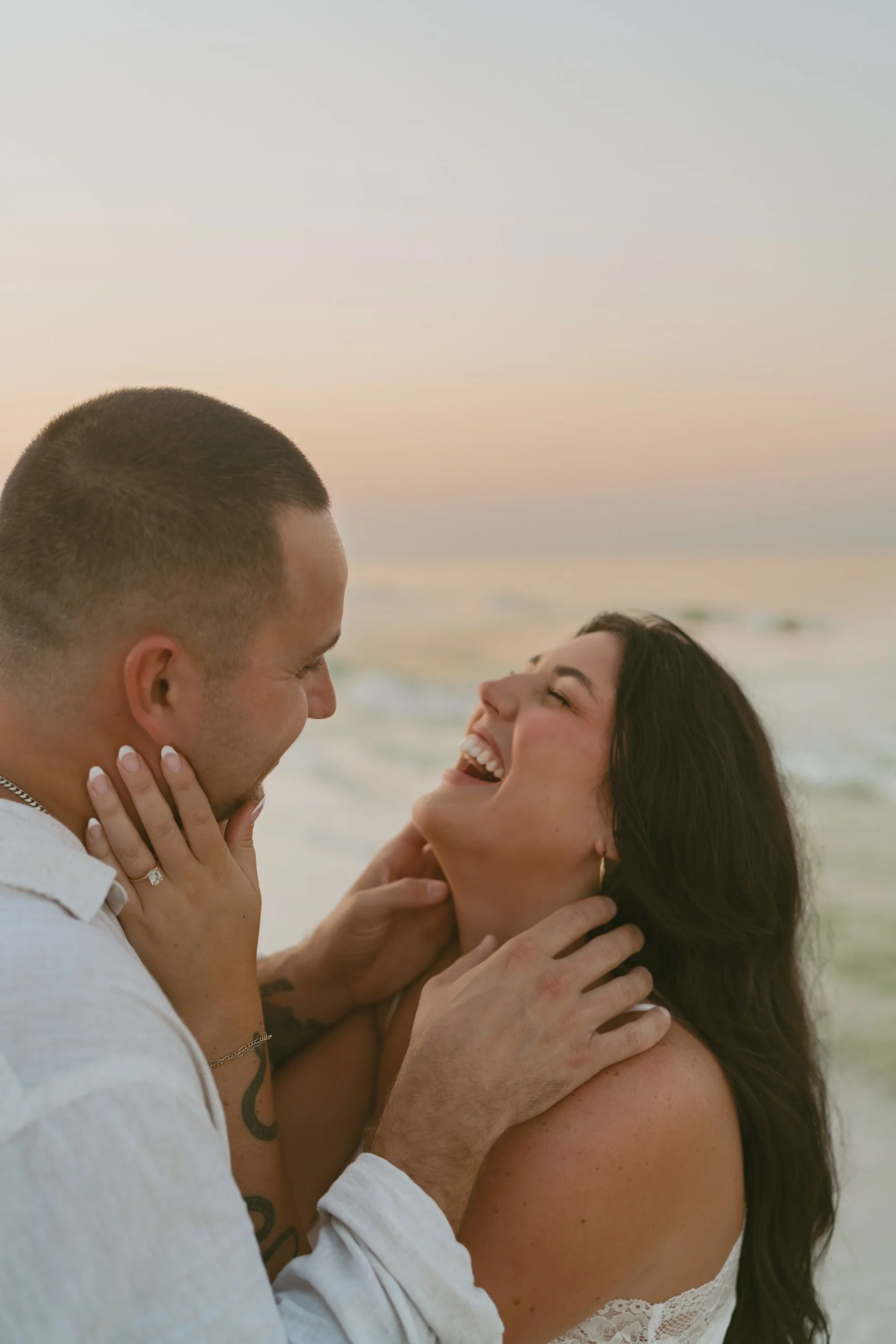 A happy couple on the beach, smiling and embracing each other during sunset.