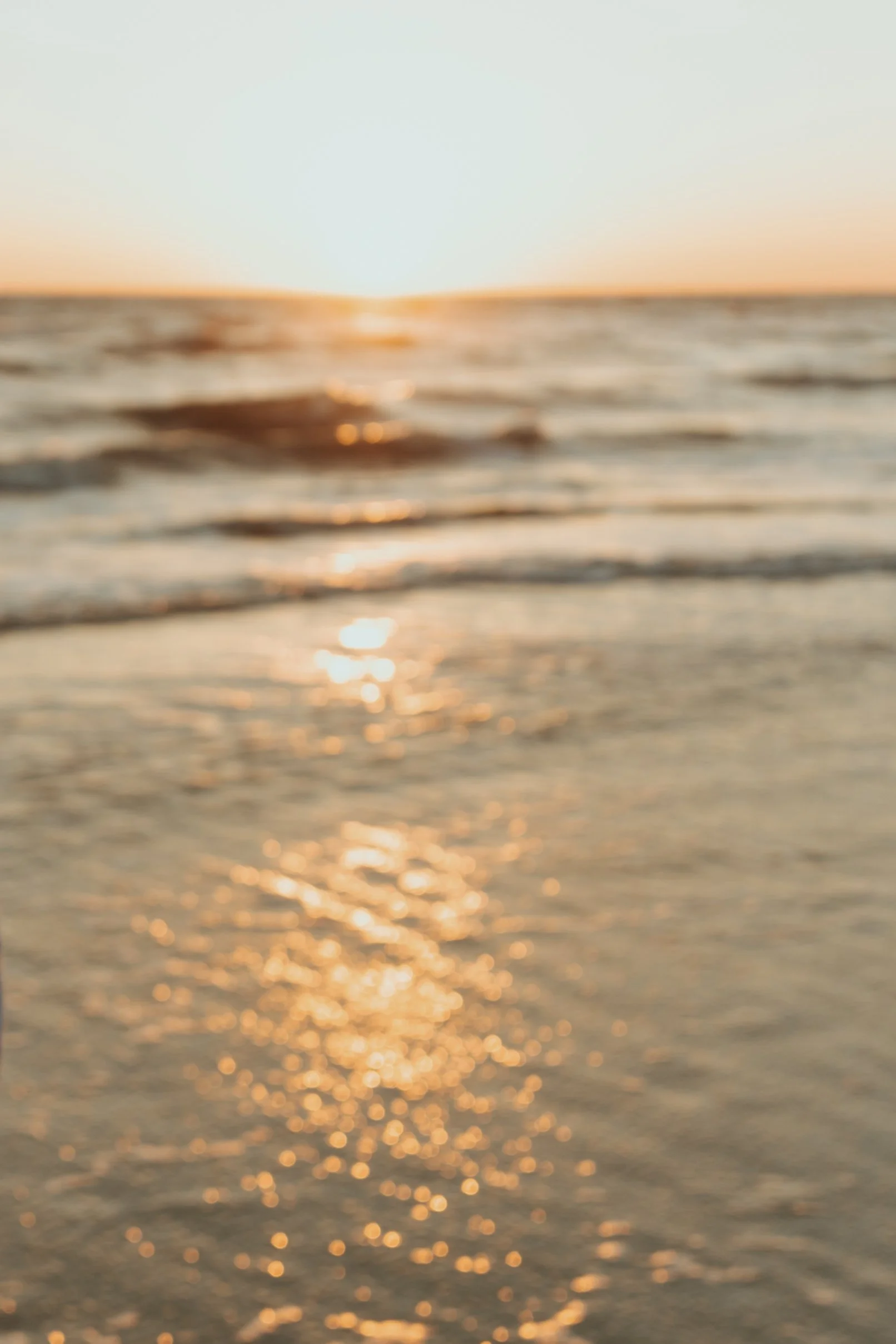 Blurred photograph of a sunset over the ocean with the sun touching the horizon, reflecting golden light on the water.