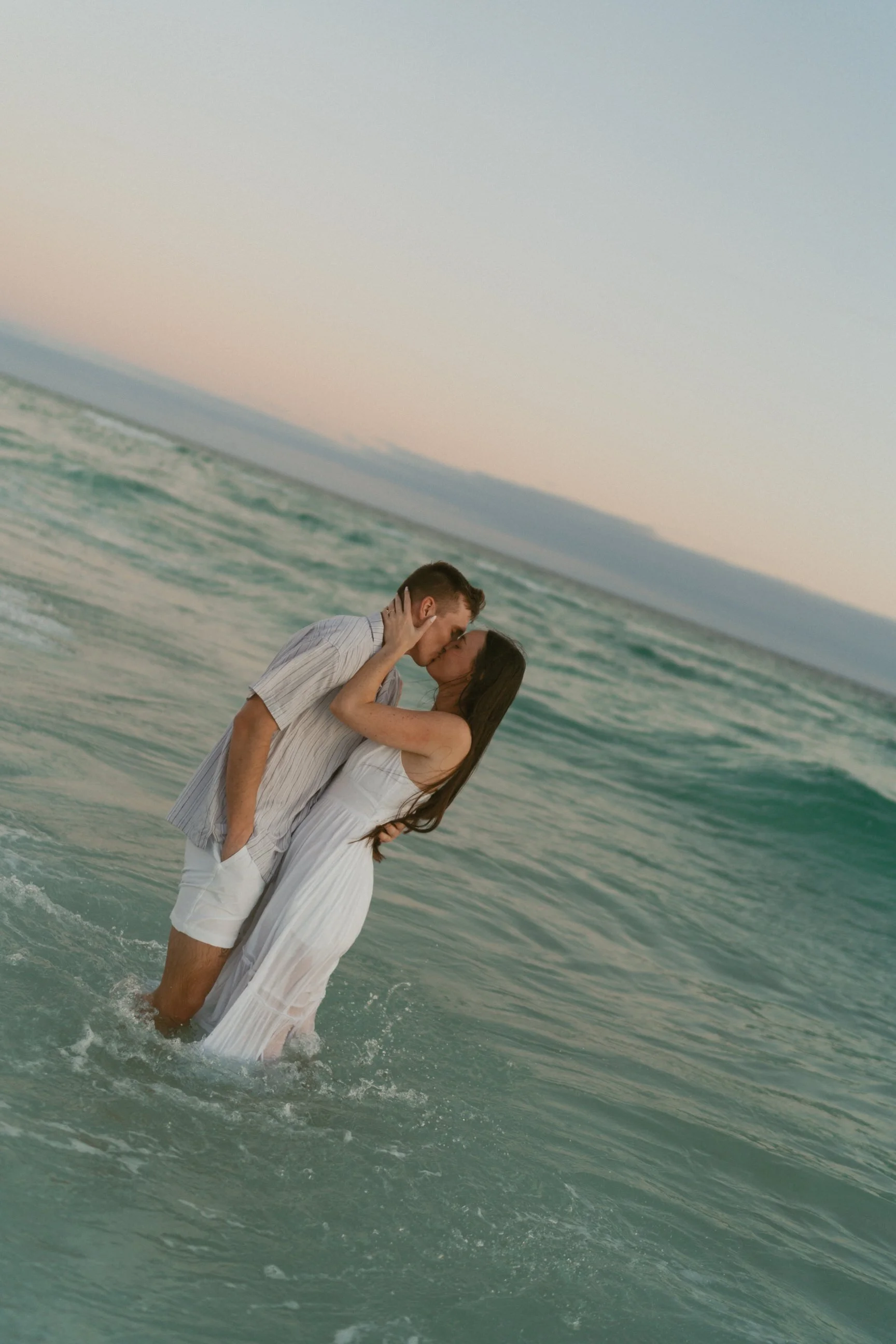 A couple standing in the ocean, about to kiss, during sunset