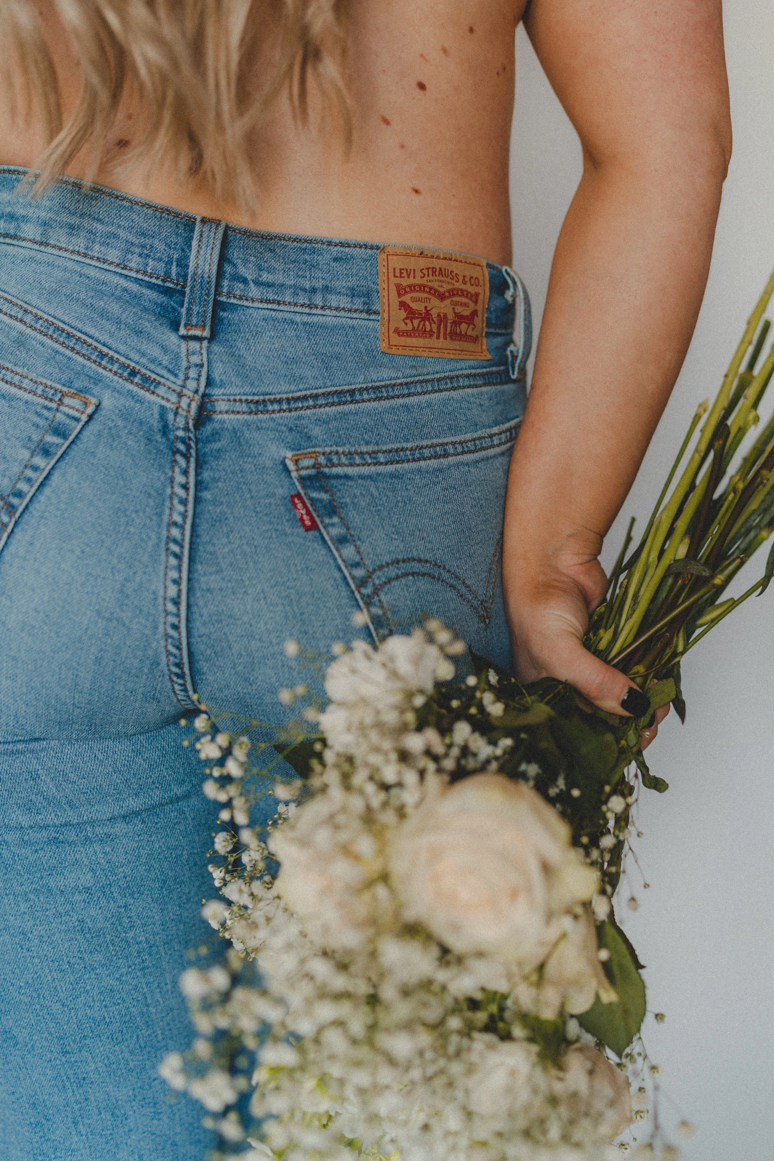 Person wearing Levi's blue jeans holding a bouquet of white flowers.