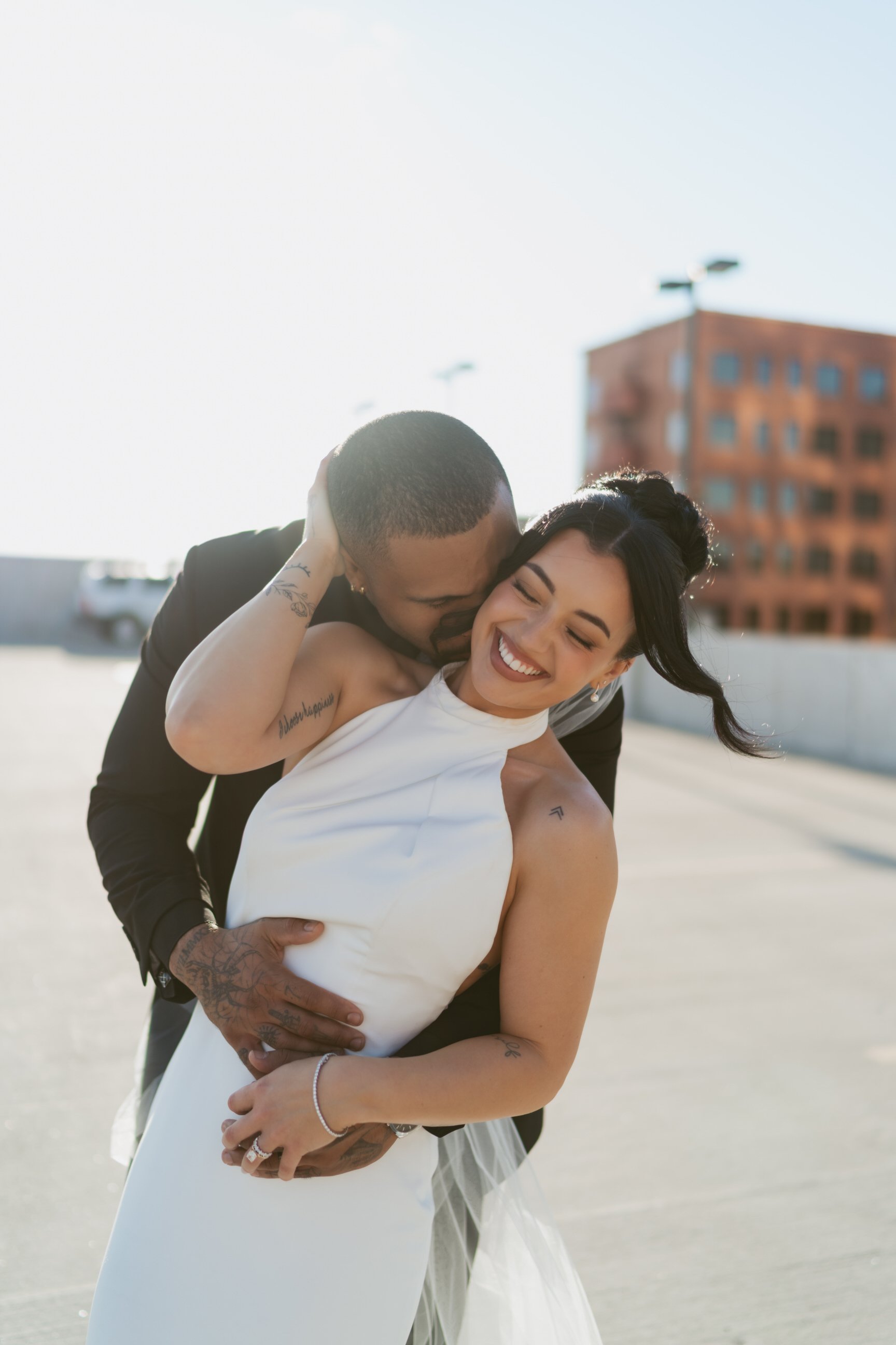 Happy couple sharing a joyful moment on top of a parking garage, with the man embracing the woman from behind and both smiling.