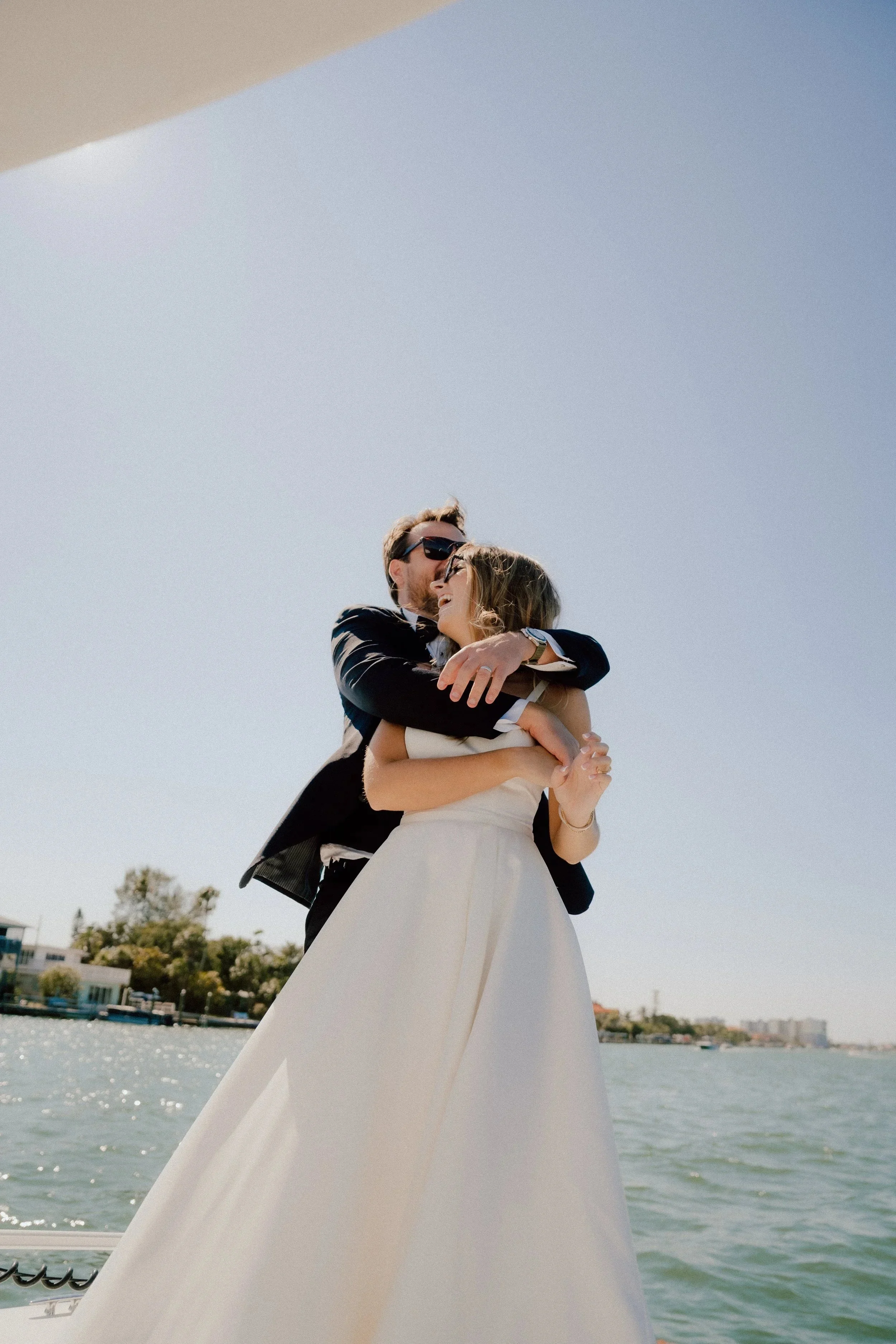 A couple embracing on a boat with water and buildings in the background, celebrating a special occasion.