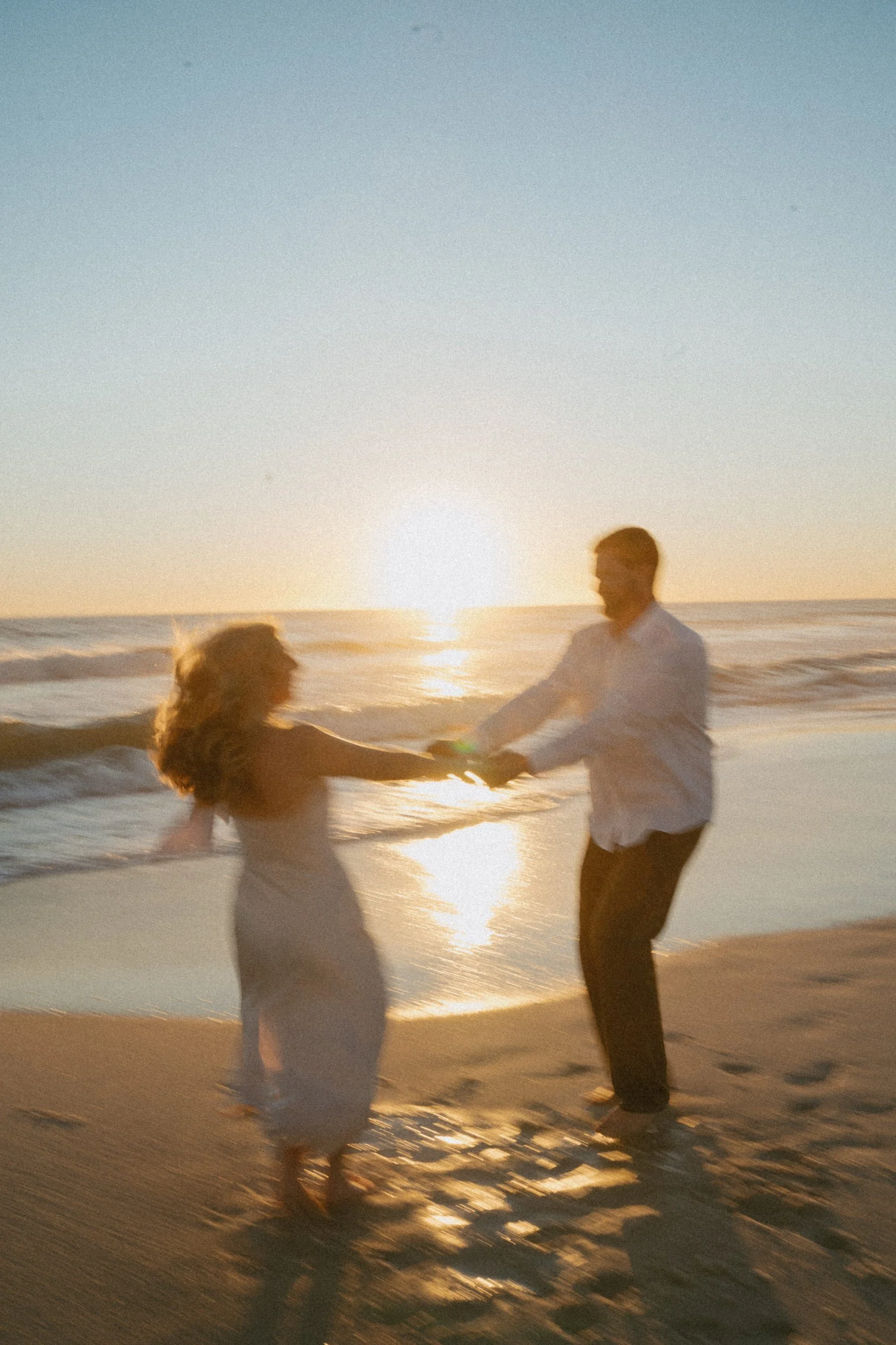 A couple dancing on the beach at sunset, holding hands and moving in a circle.