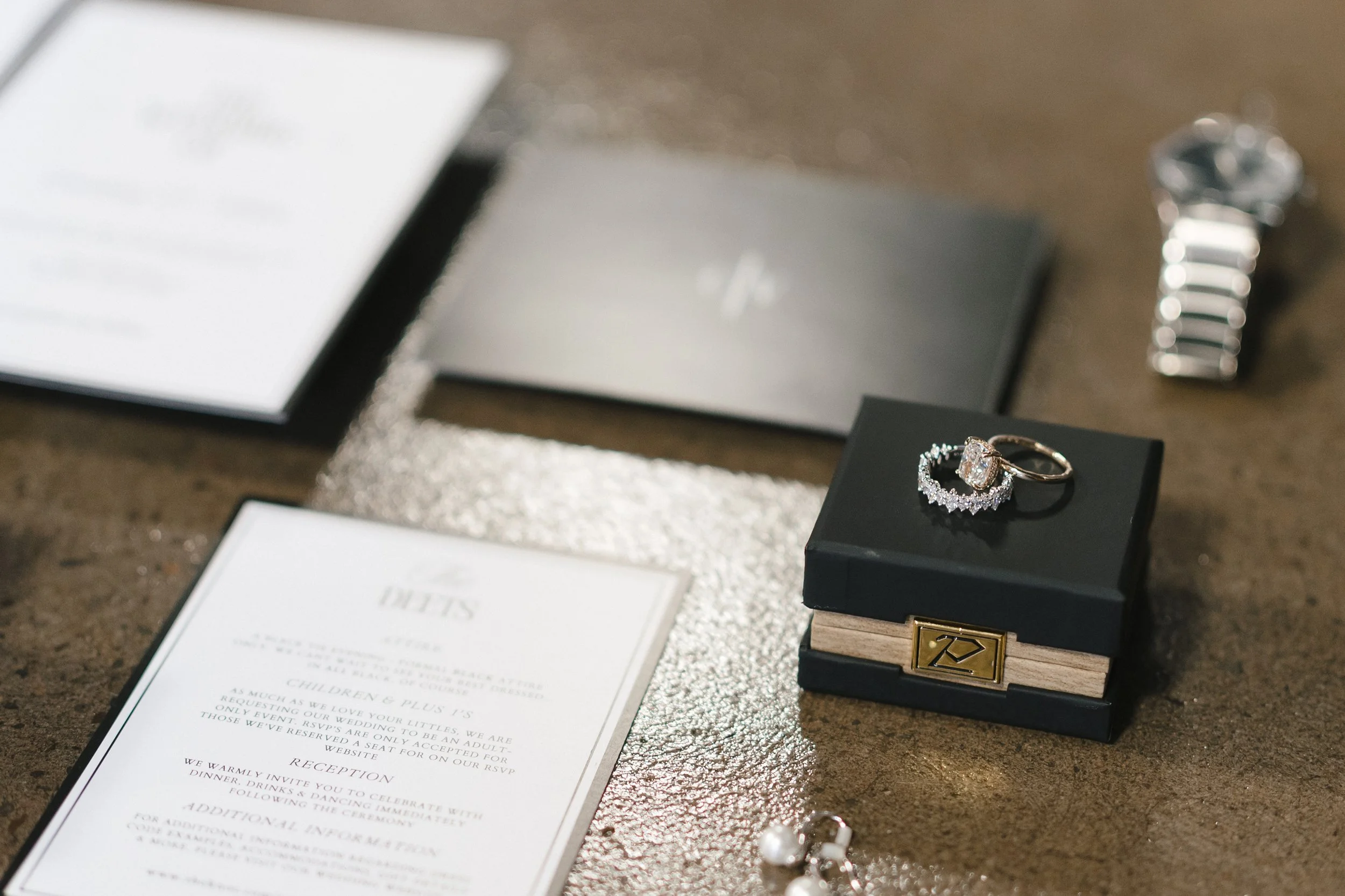  flatlay of wedding day details including the invitation suite, watch, rings, and ceremony newspaper  