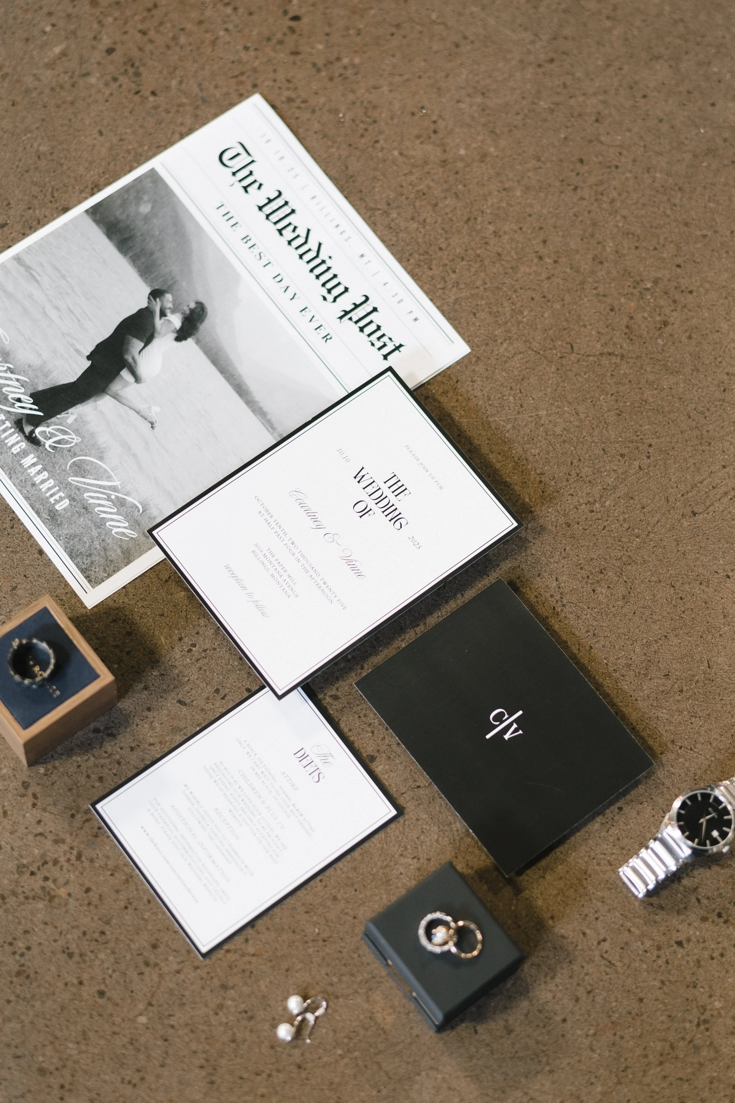  flatlay of wedding day details including the invitation suite, watch, rings, and ceremony newspaper  