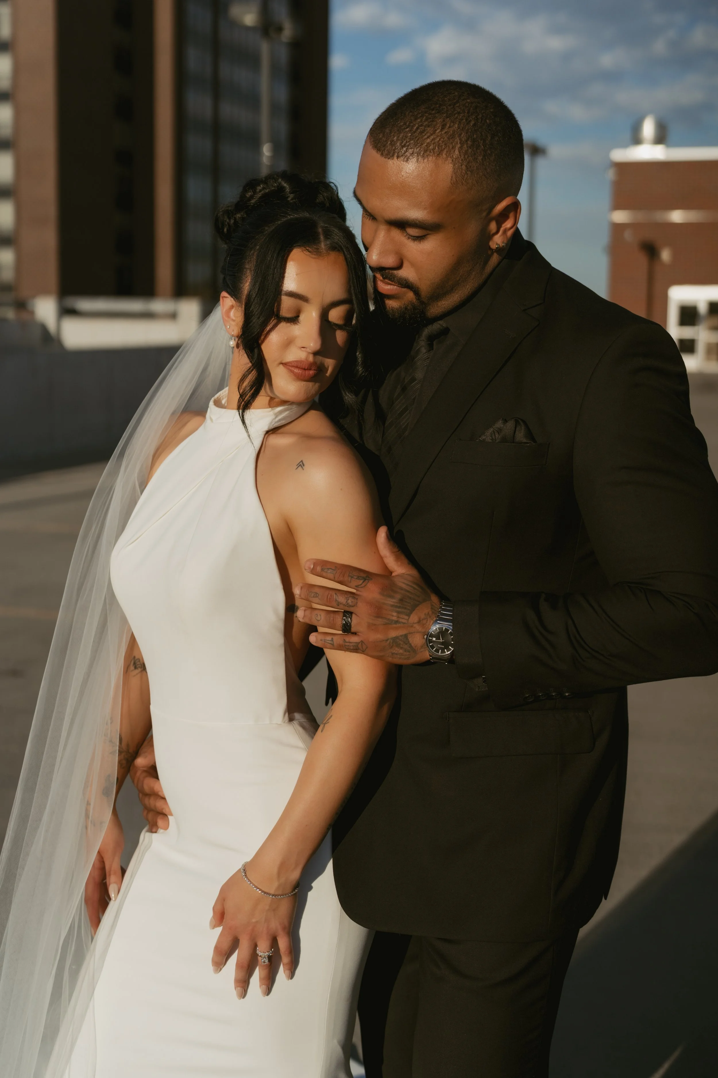  Bride and groom for romantic portraits on their wedding day he is looking at her and she is looking over her shoulder while he caresses her arm  