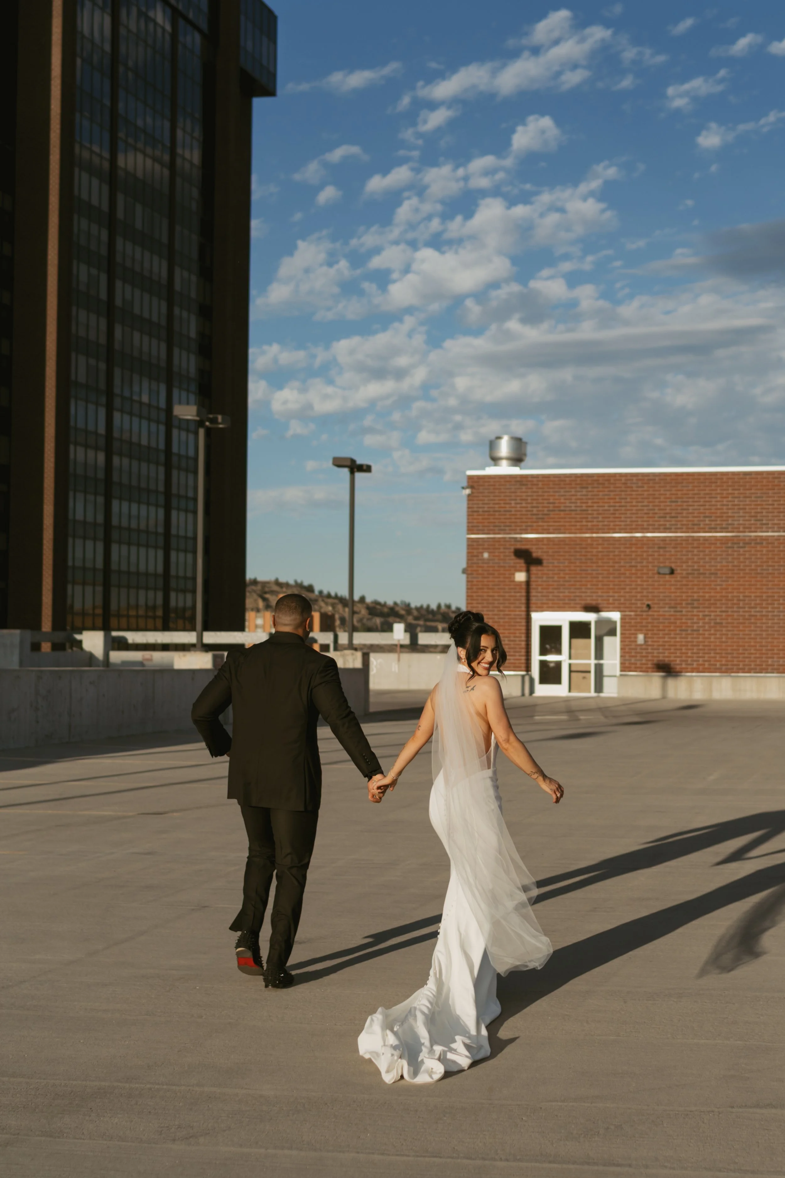  bride and groom running back to the car after wedding portraits laughing together on a rooftop of a parking garage bride looking back smiling  
