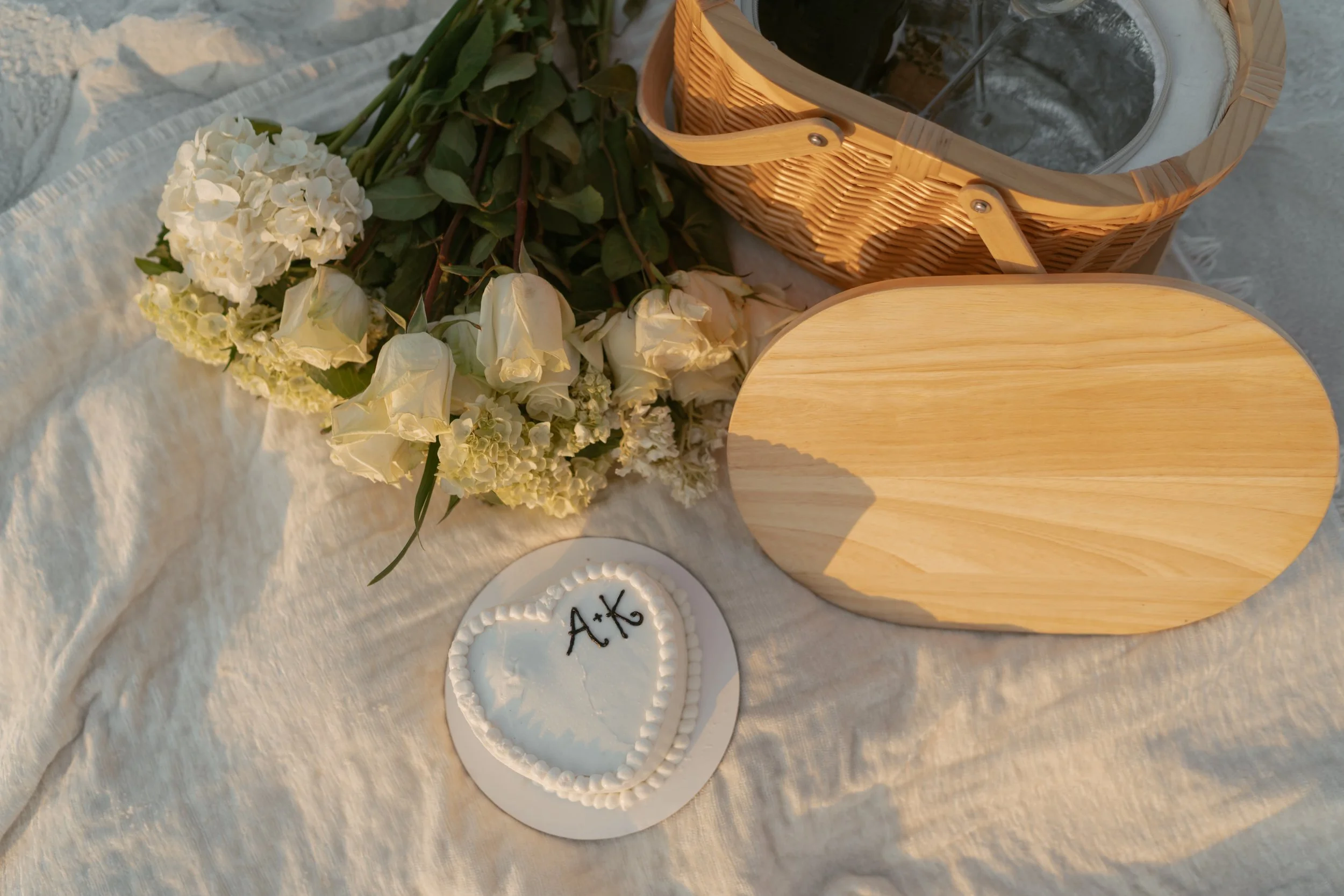Engagement photo details on the beach, picnic basket, cake with couples initials and a bouquet of flowers