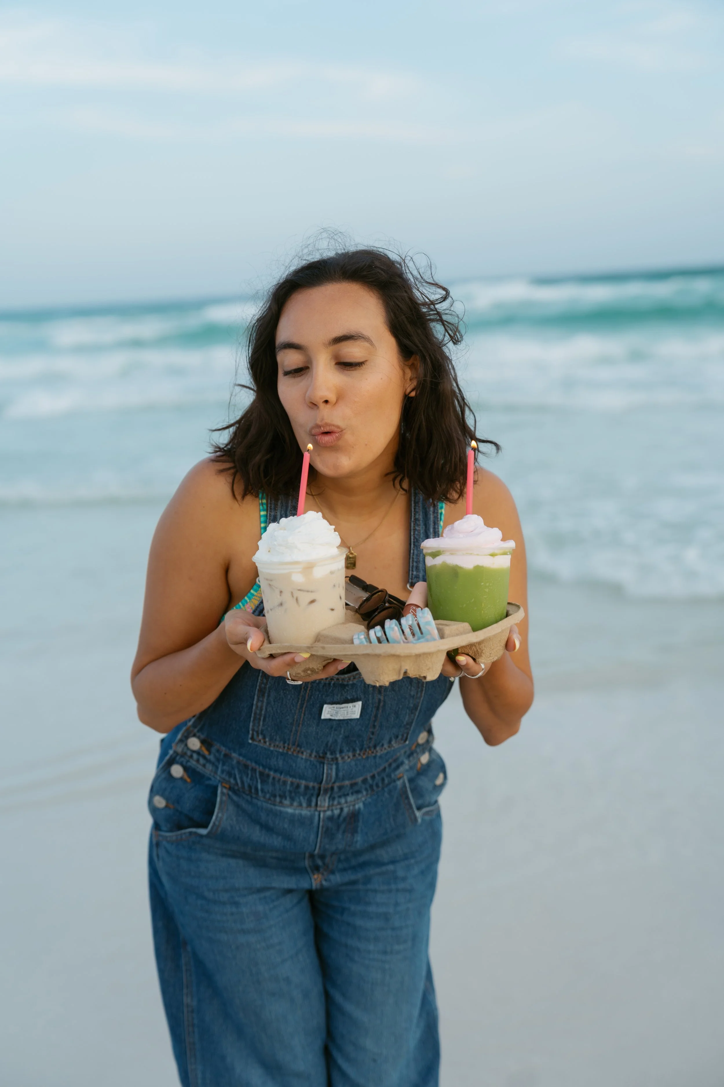  girl in overalls blowing out candle on a latte that is topped with whip cream 