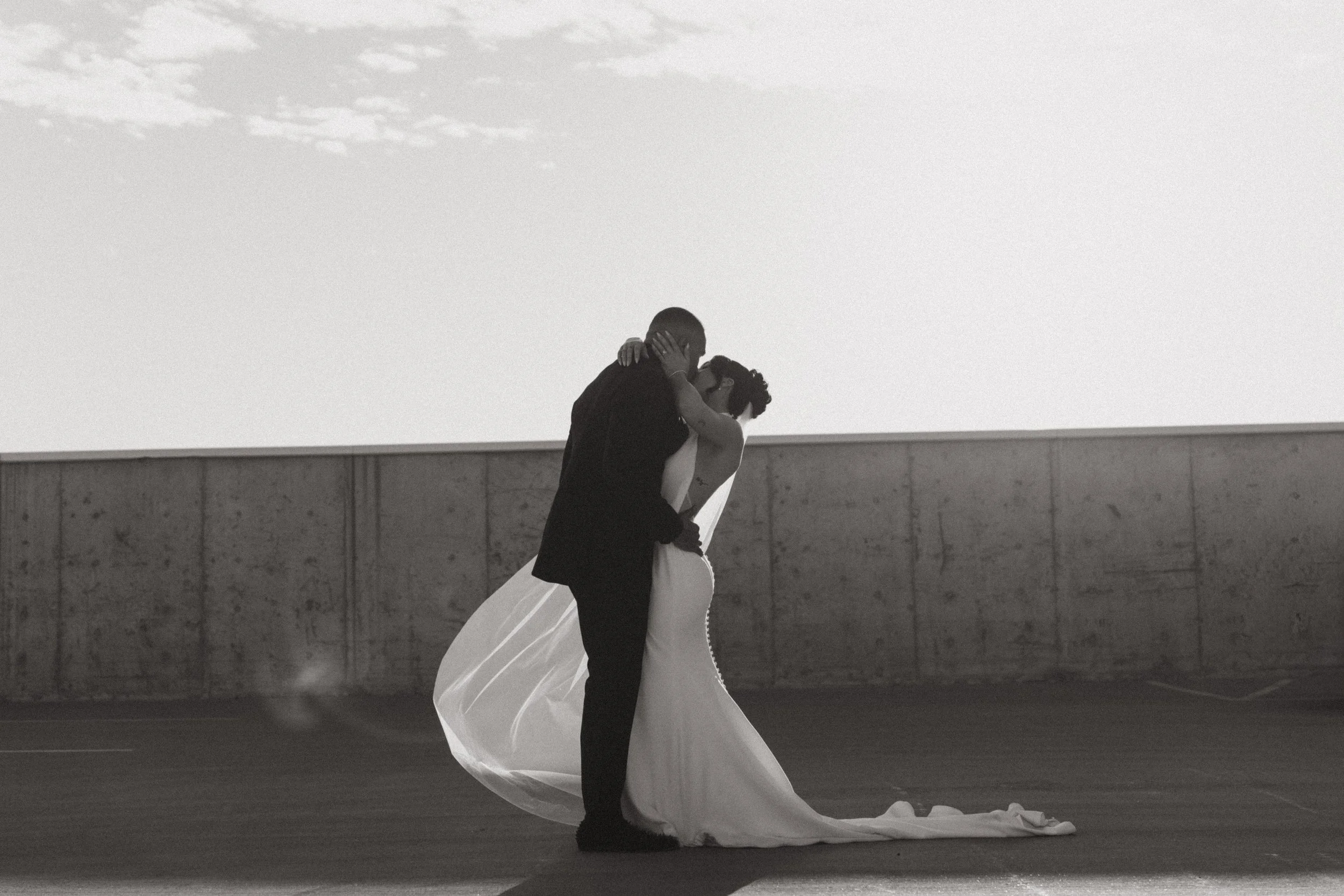 Romantic black and white photo of bride and groom kissing during their wedding portraits with her veil blowing in the wind