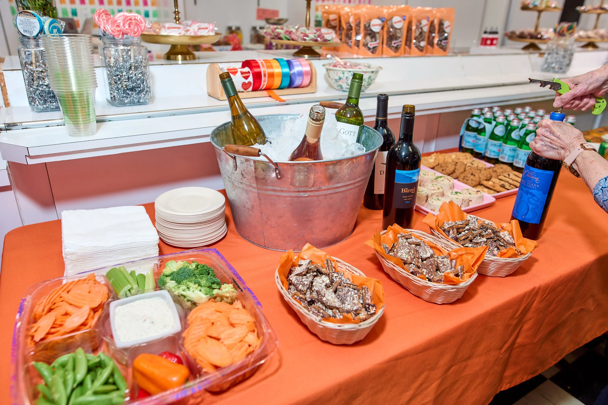 Table covered with an orange tablecloth, with an assortment of drinks and snacks