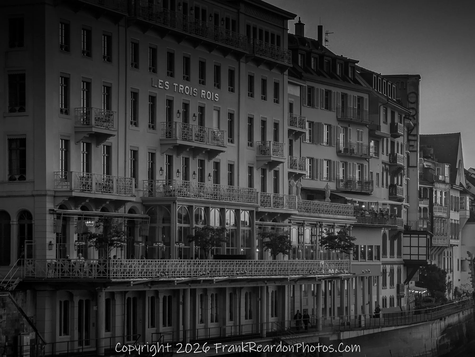 "Les Trois Rois at Dusk" A black-and-white image of the grand Les Trois Rois hotel facade, highlighting the intricate balconies and architecture along the riverfront.