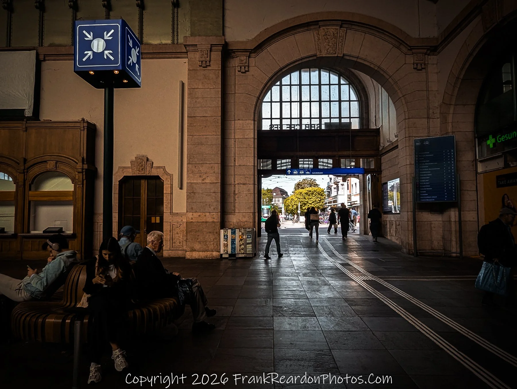 “Convergence Point”
The image captures the essence of movement and pause — travelers crossing paths beneath the meeting-point symbol, framed by the grand archway that opens to the city beyond.