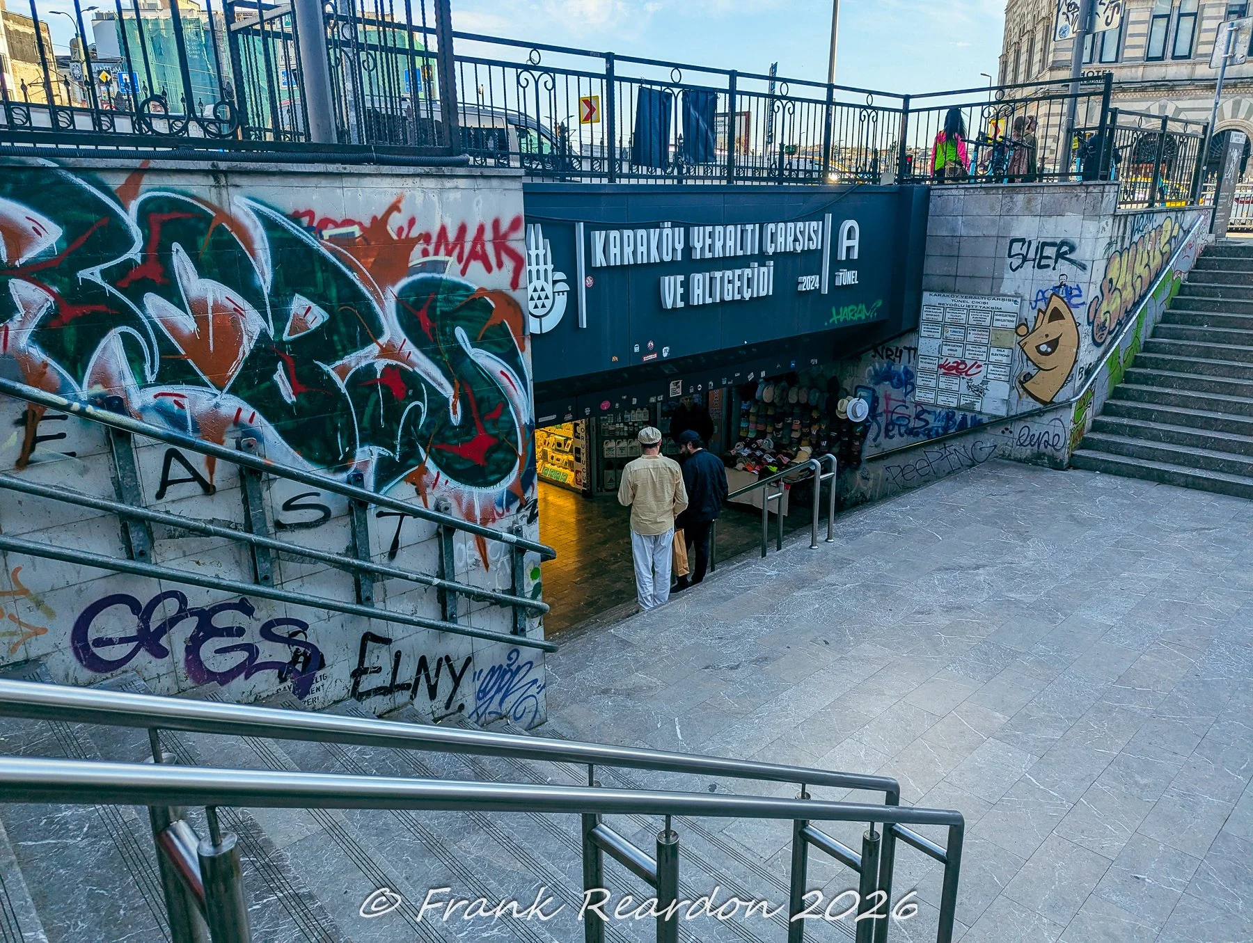 Pedestrians entering the Karaköy Underground Passage and Underpass (Karaköy Yeraltı Çarşısı ve Altgeçidi), surrounded by concrete walls covered in vibrant urban graffiti.