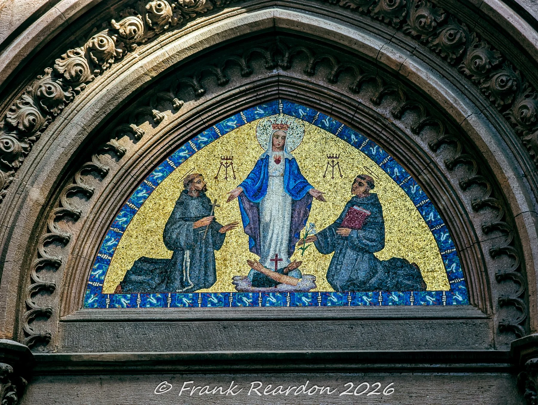 A detailed close-up of the colorful mosaic lunette above the entrance portal of the Church of Saint Anthony of Padua, depicting religious figures against a golden backdrop.