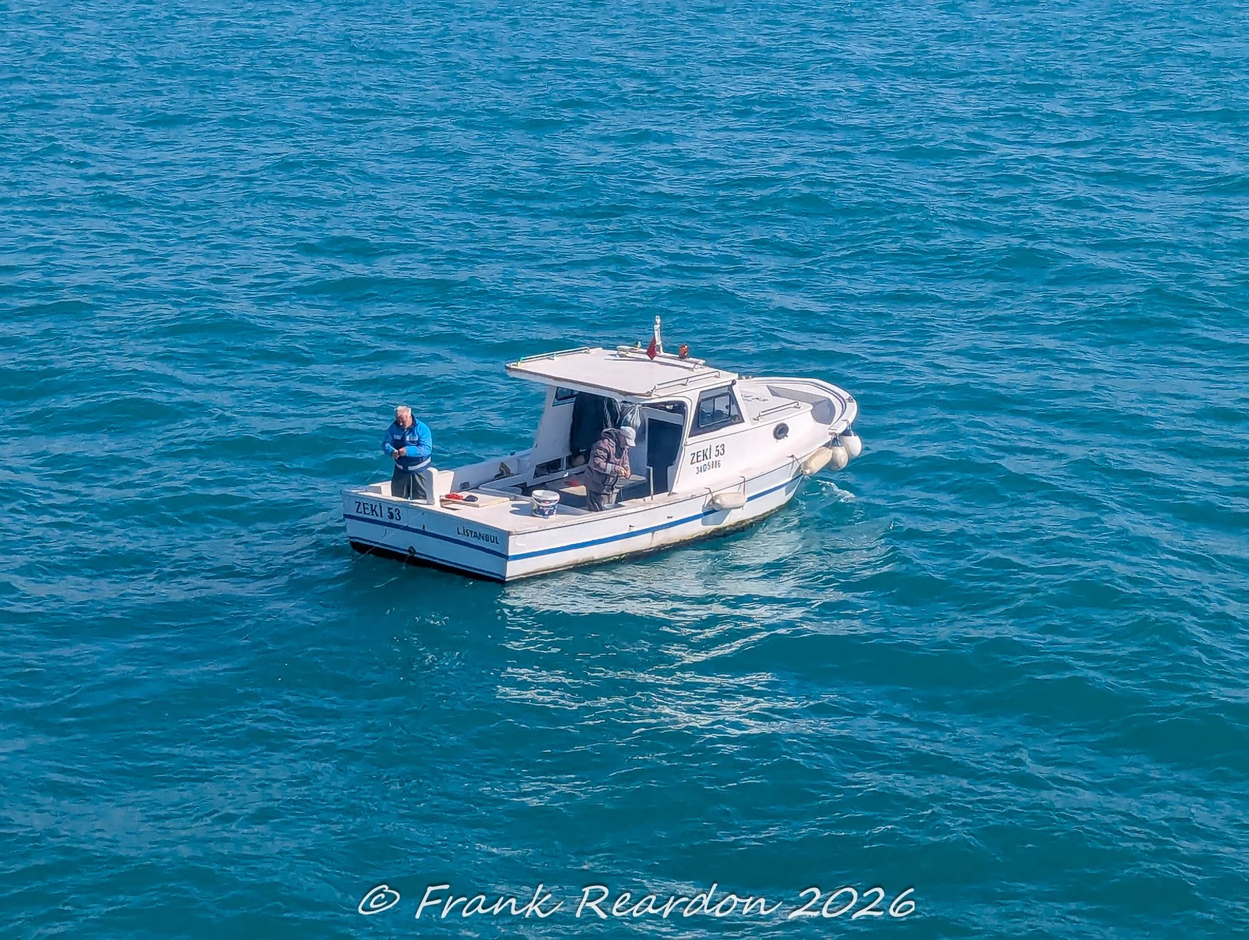 A high-angle action shot of a small local fishing boat named Zeki 53 navigating the deep blue waters of the Bosphorus strait.