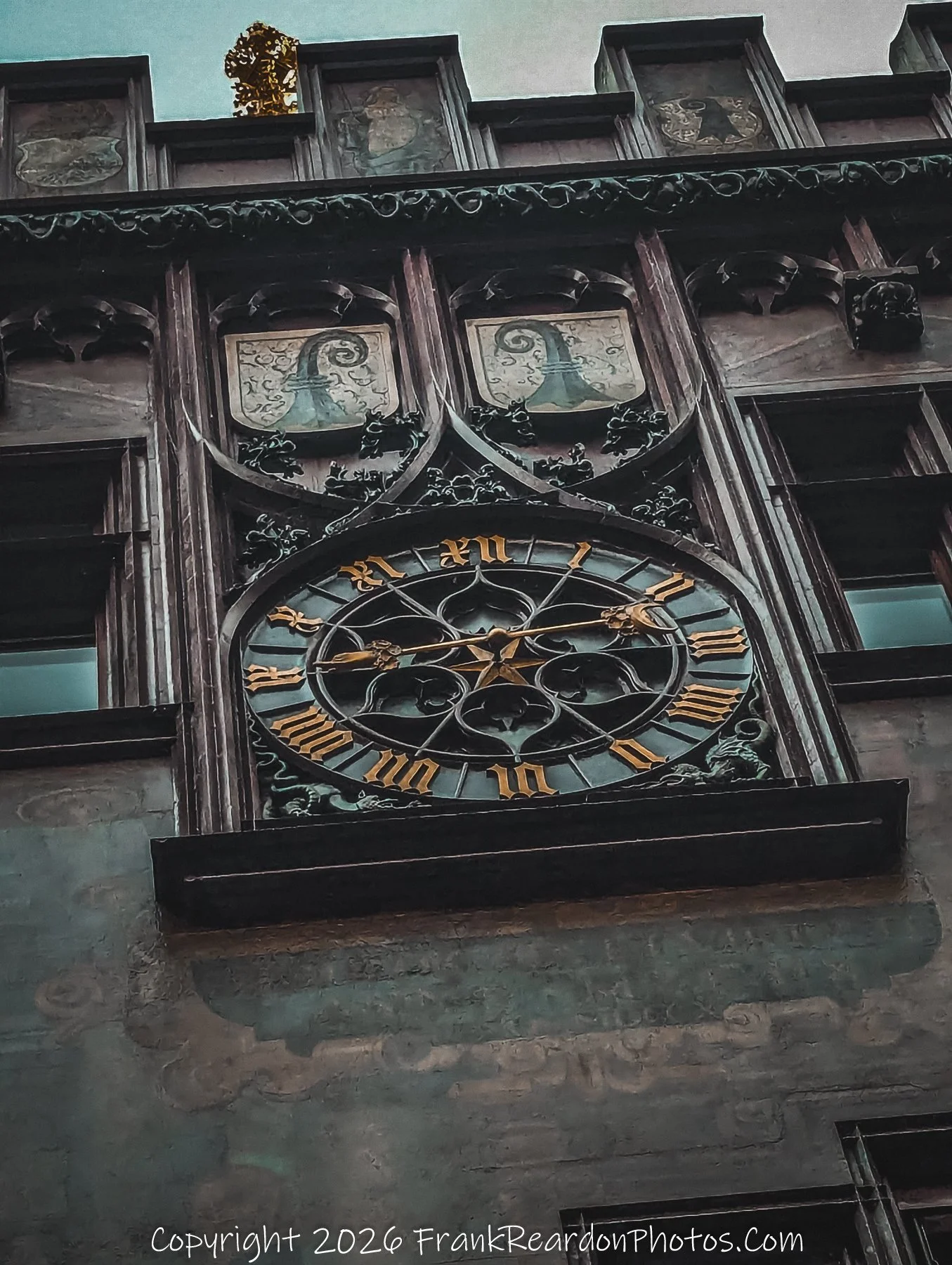 "Clockwork Heritage" A low-angle, detailed shot of an ornate, dark-toned historic clock face mounted on a building facade, accented with gold Roman numerals and architectural crests.