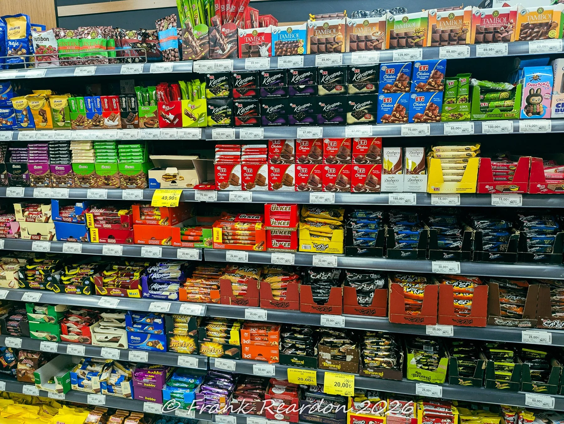 Shelves inside a Turkish market filled with rows of local chocolates, wafers, and sweet treats including brands like Ülker and Eti.