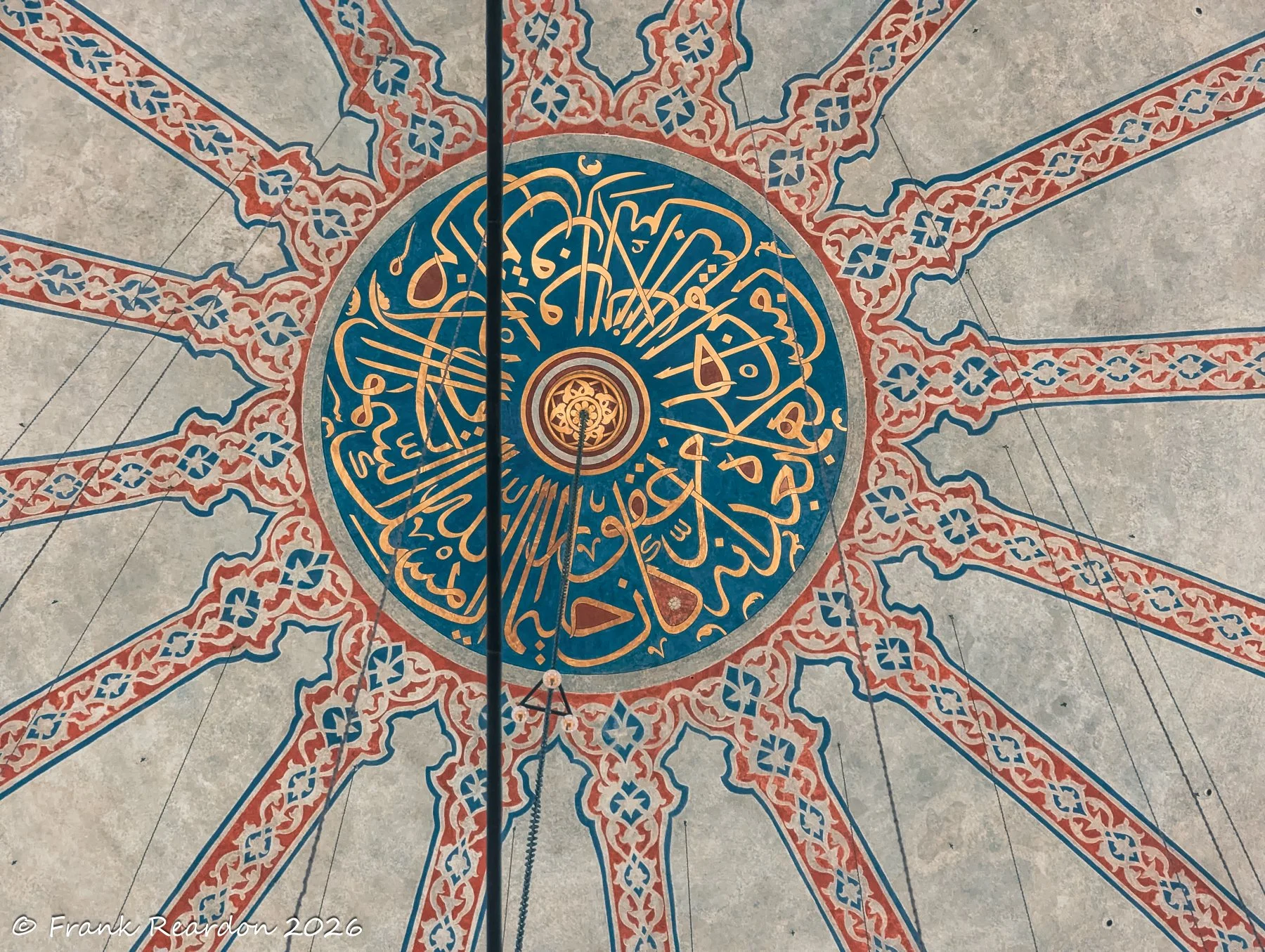 A close-up look at a large circular medallion featuring golden Arabic script set against deep blue and red geometric tilework.