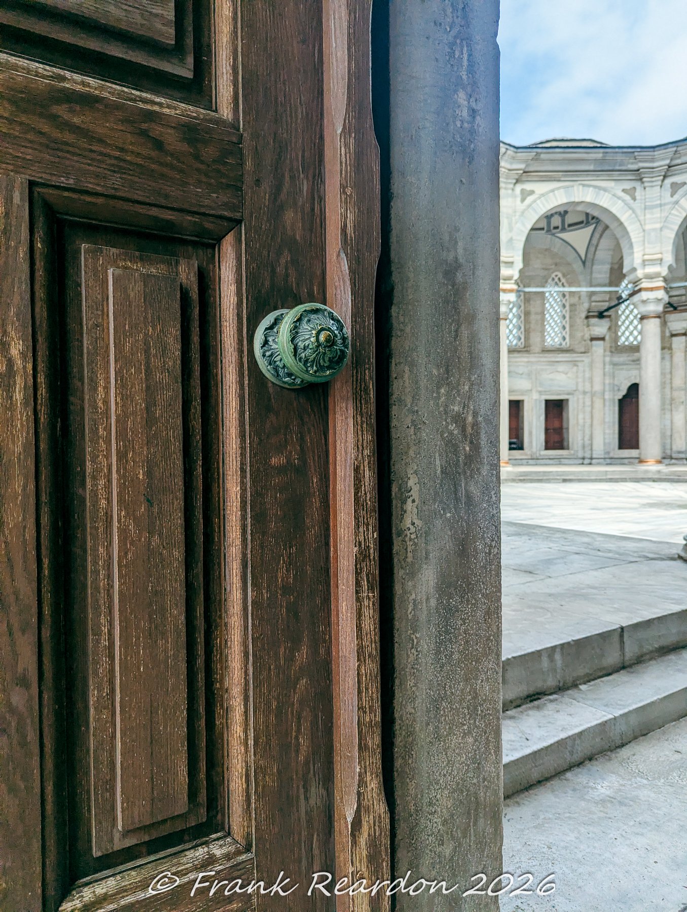 A close-up perspective of a weathered wooden panel door with a decorative green-patina metal knob at the Nuruosmaniye Mosque.