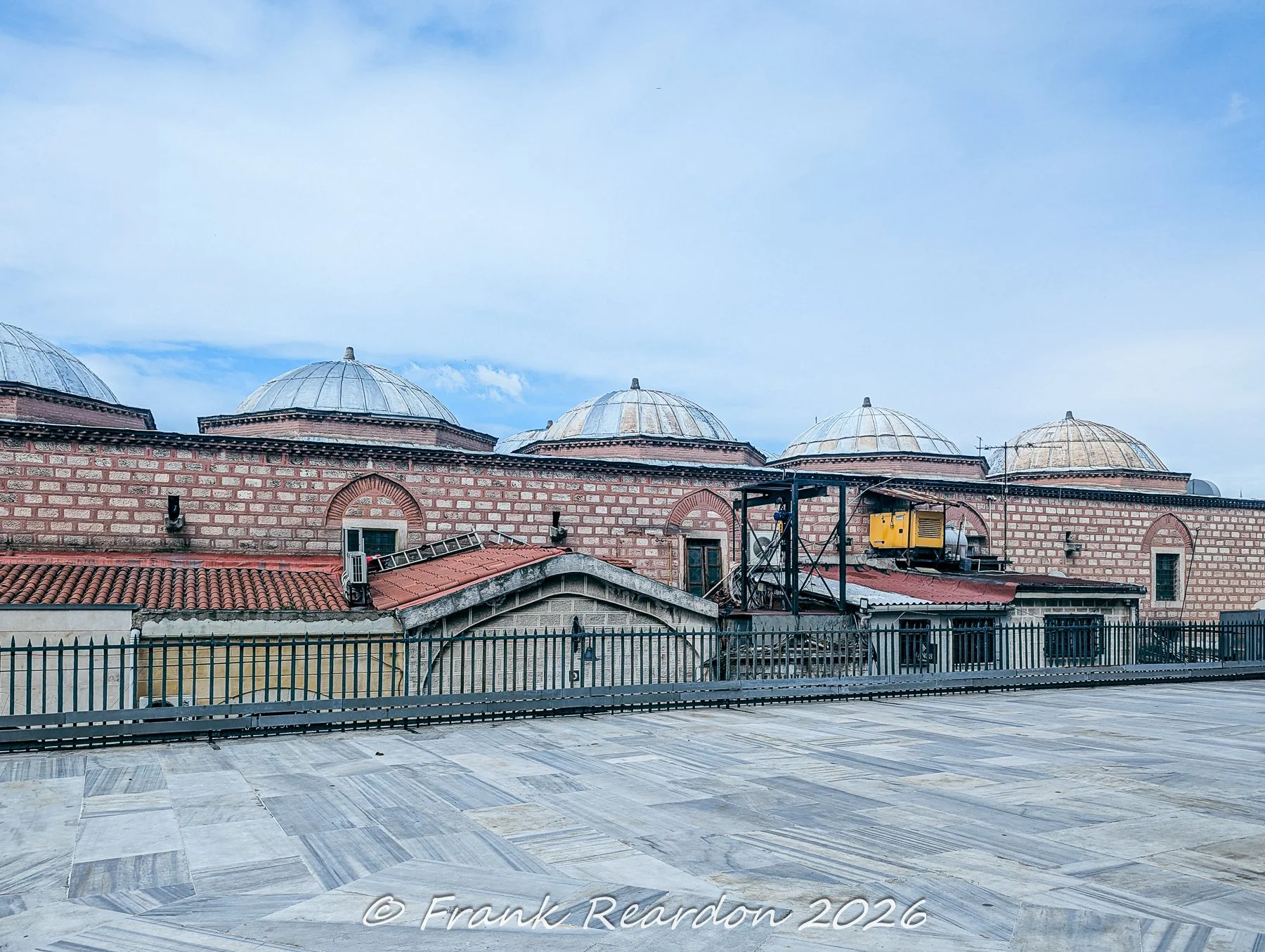 A wide view looking across the marble courtyard of the Nuruosmaniye Mosque toward the historic brick domes and terracotta tile roofs of the surrounding district.