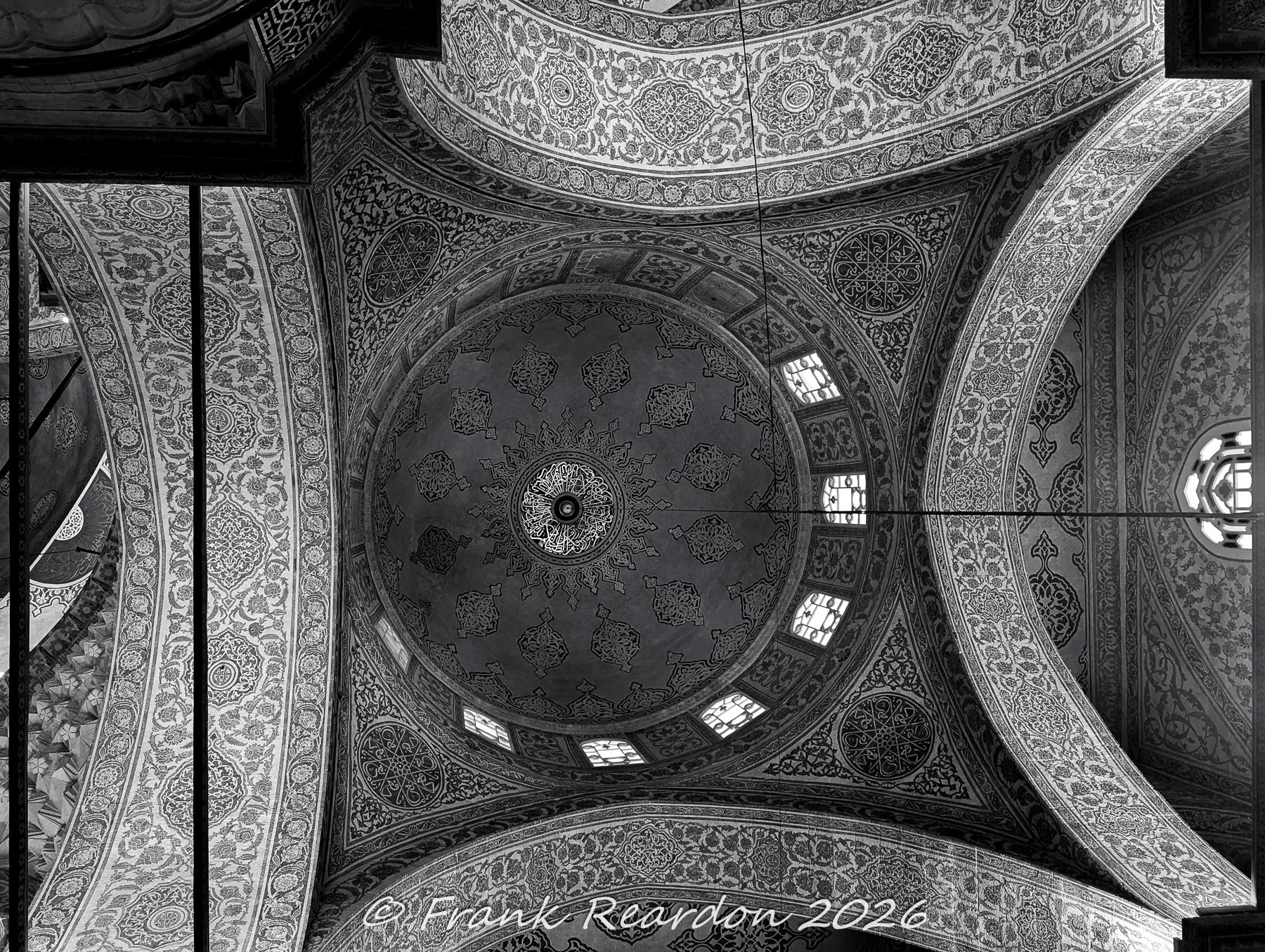 A detailed black-and-white upward view of the heavily patterned arabesque tilework and vaulted arches inside the Sultan Ahmed Mosque (Blue Mosque)