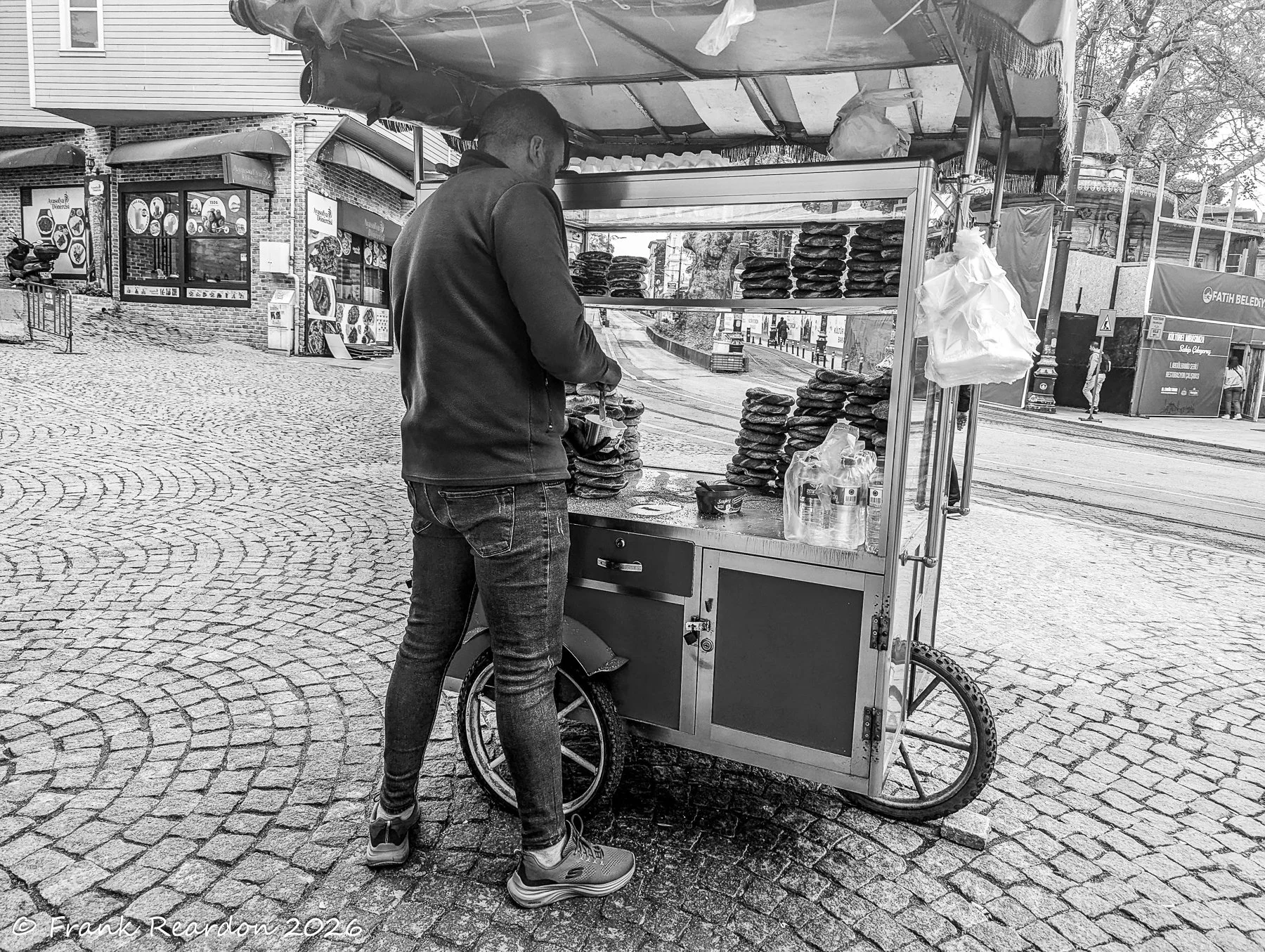 A street vendor tending to a mobile cart stacked with traditional baked goods on a cobblestone street in Istanbul.